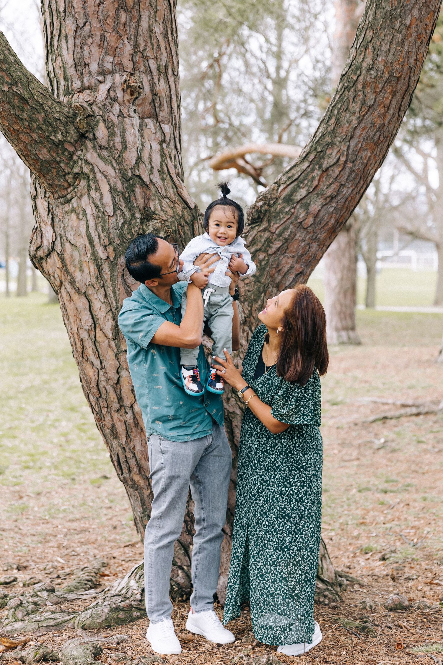 A family poses together by a large forked tree trunk in a park.