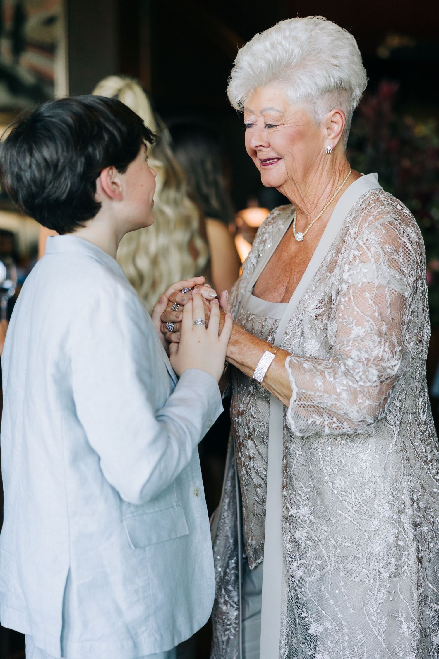 Two people share an emotional moment at a formal event, with one wearing a delicate silver lace dress.