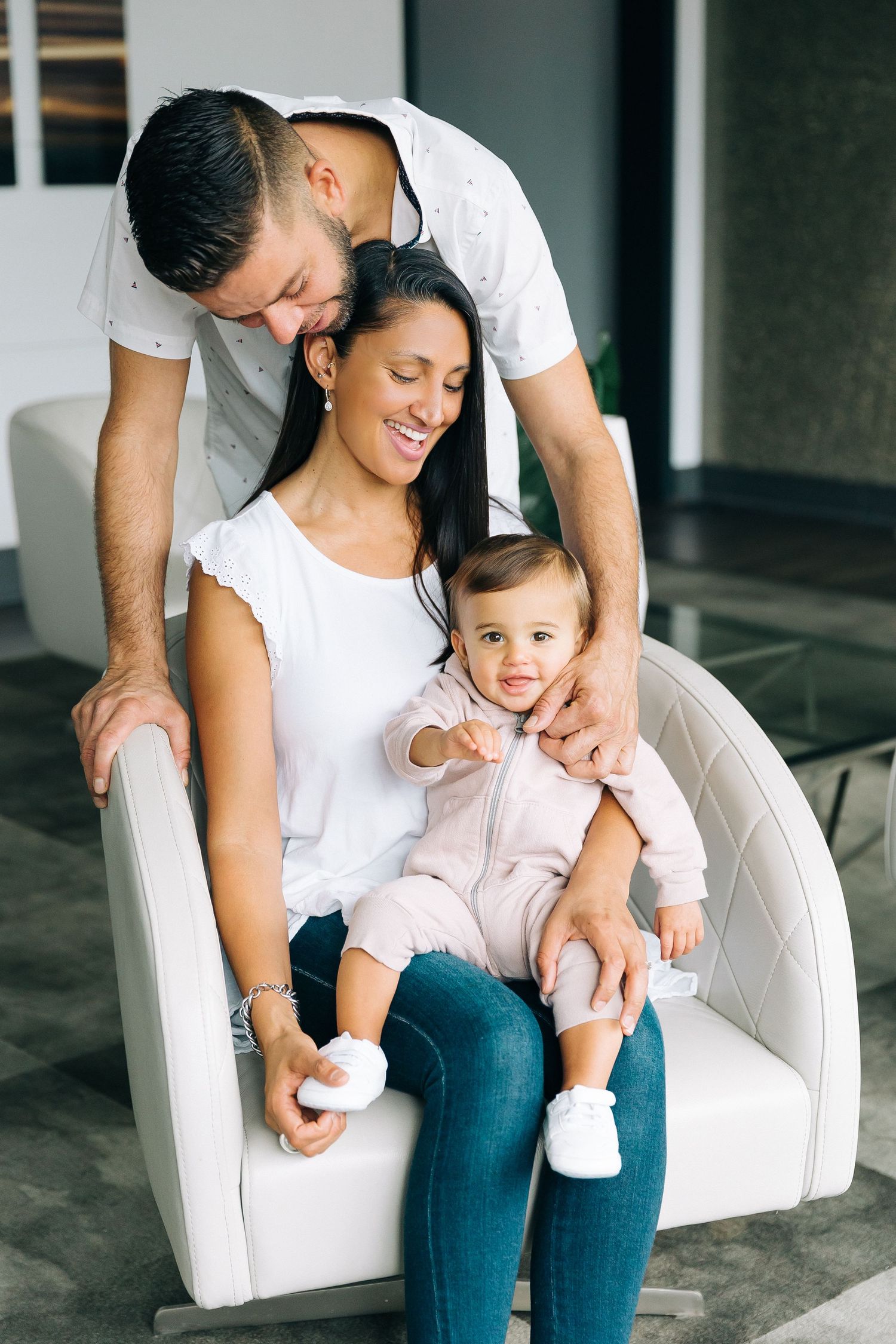 A family shares an intimate moment while sitting together in a white upholstered chair.