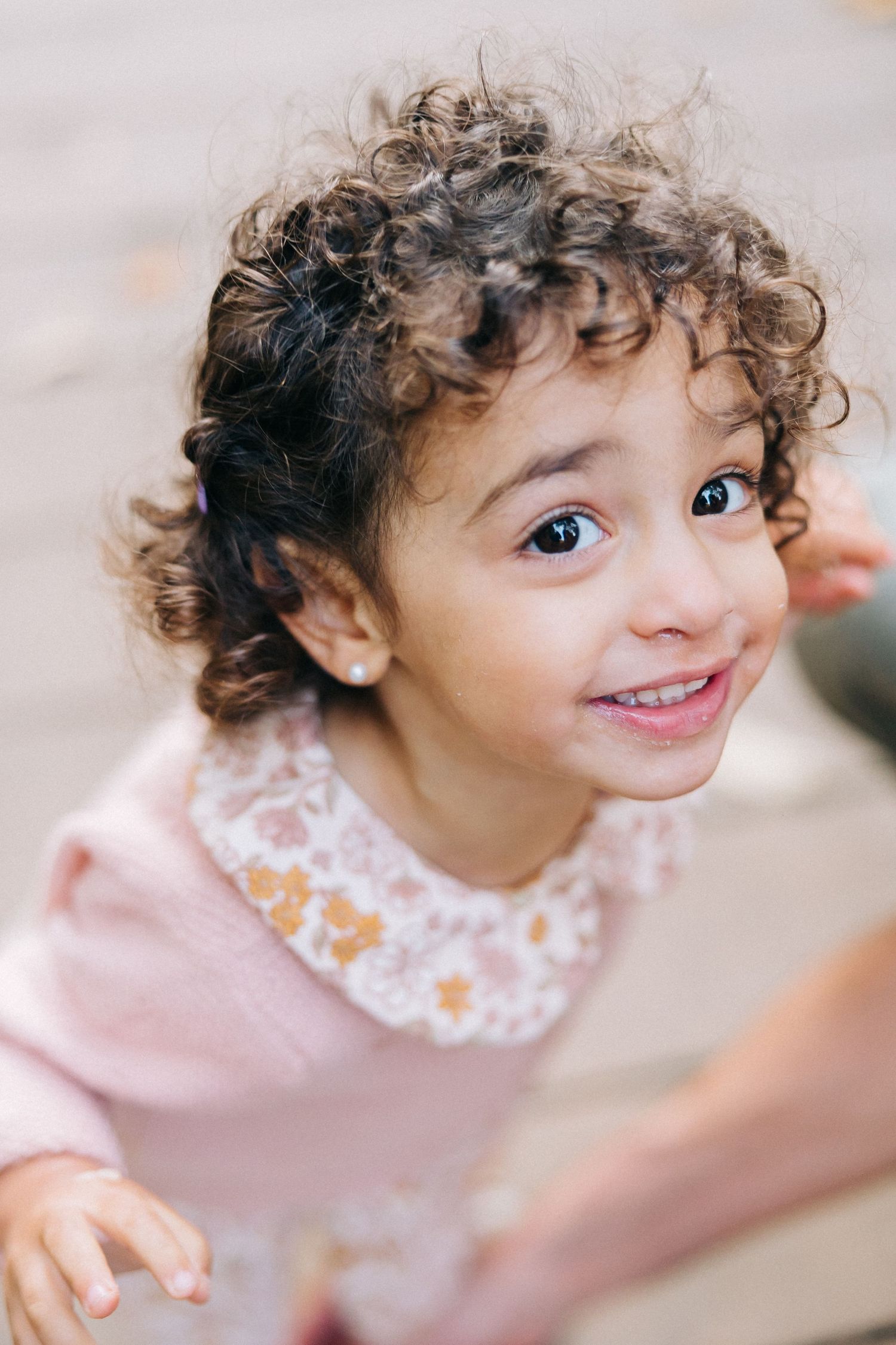 Close up portrait of a smiling child with curly hair wearing a pink collared top.