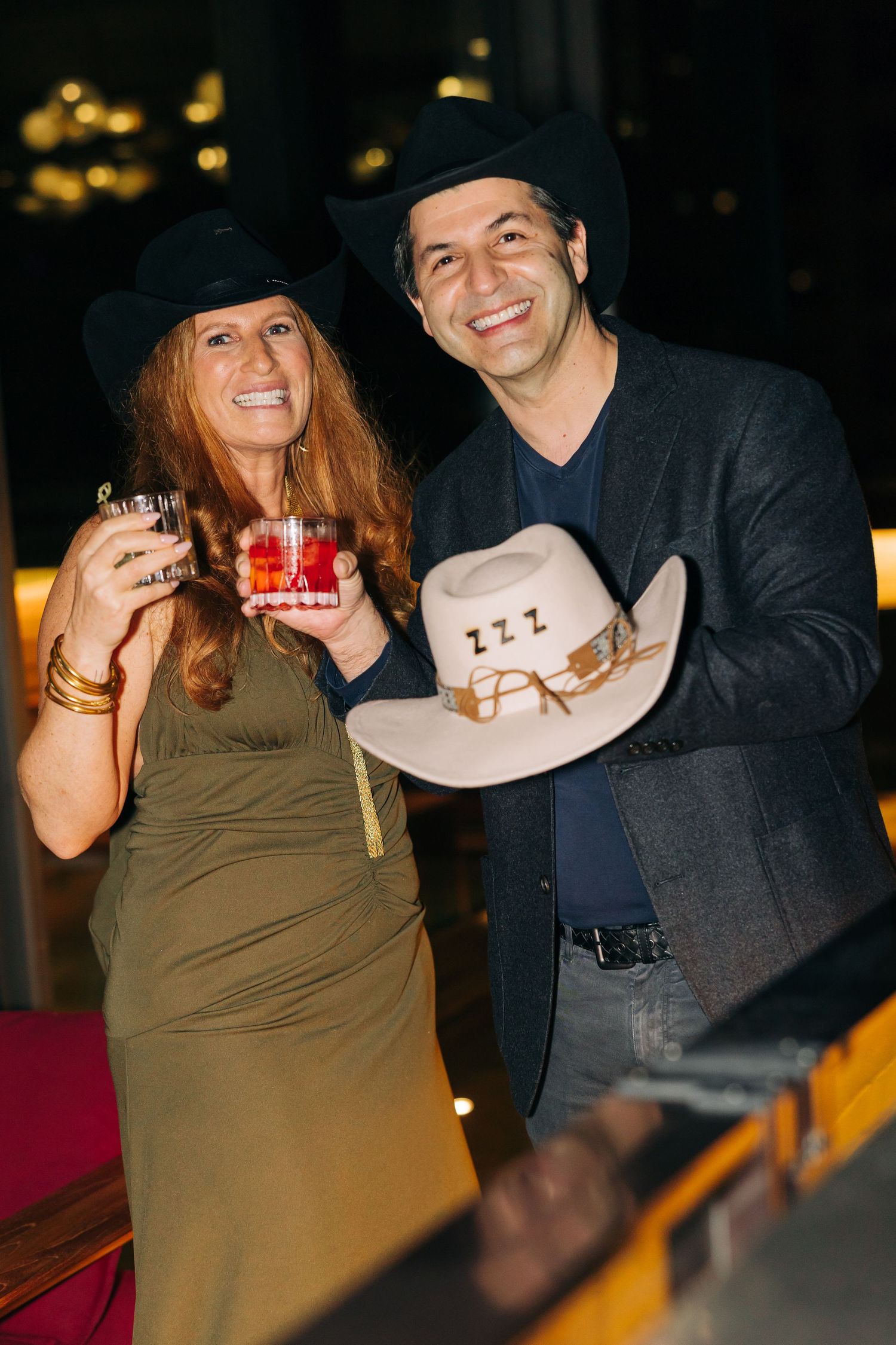 Social gathering scene with people holding drinks and a cowboy hat.