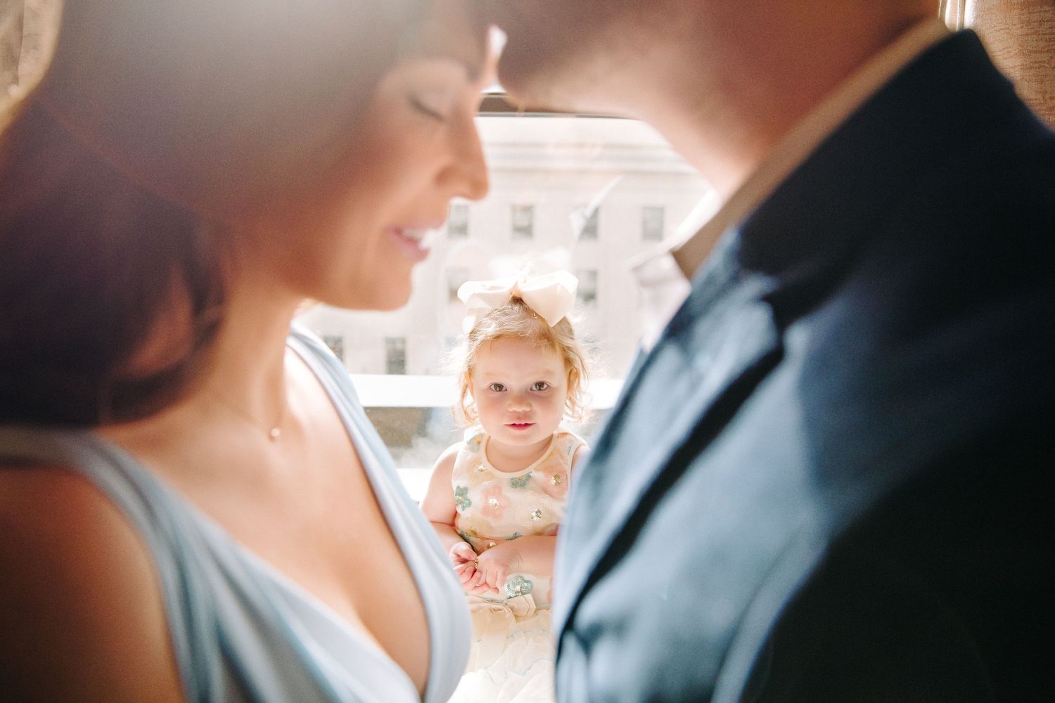 Couple in foreground with baby peeking through in soft focus background.
