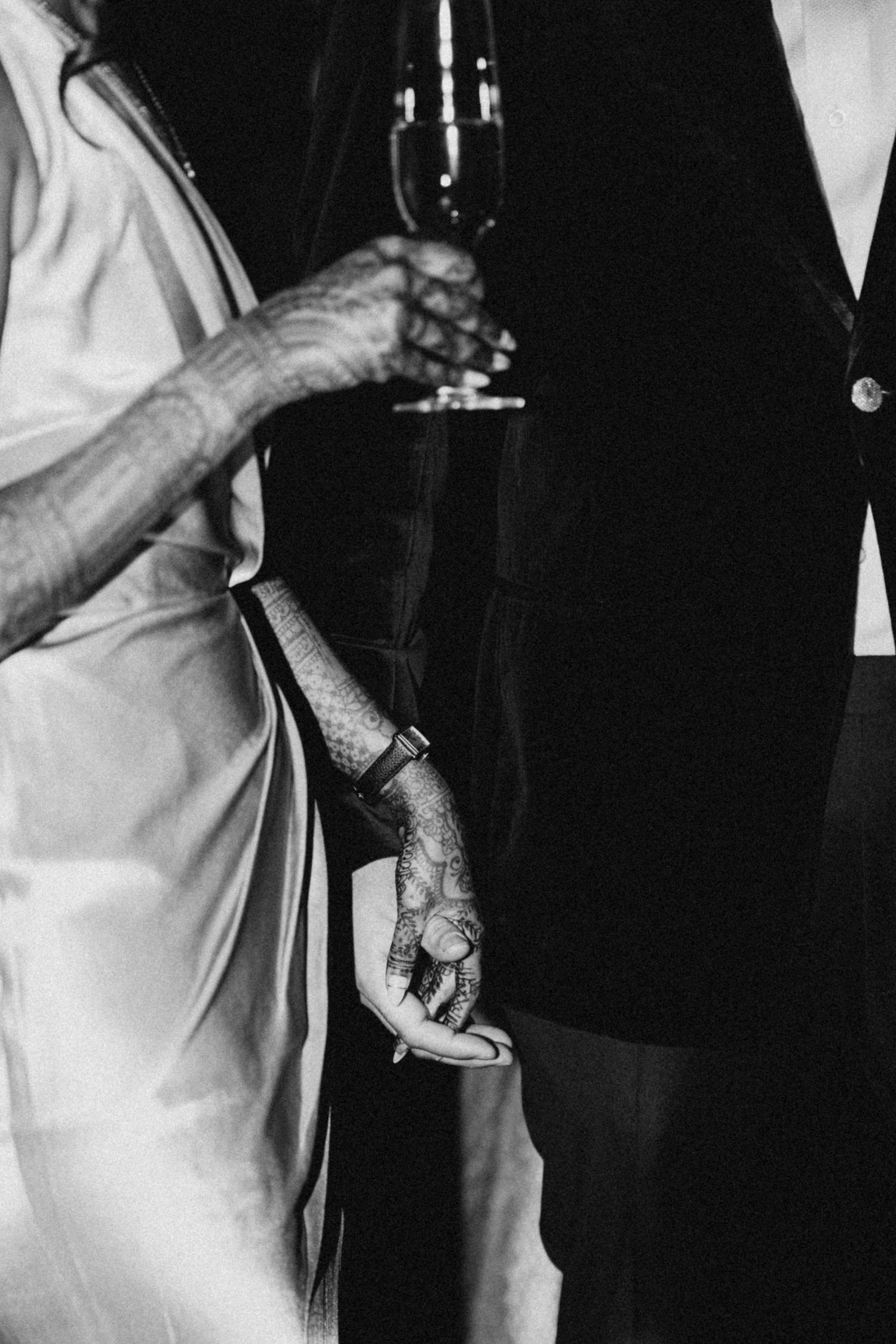 A black and white closeup of hands holding champagne glasses in formal attire.