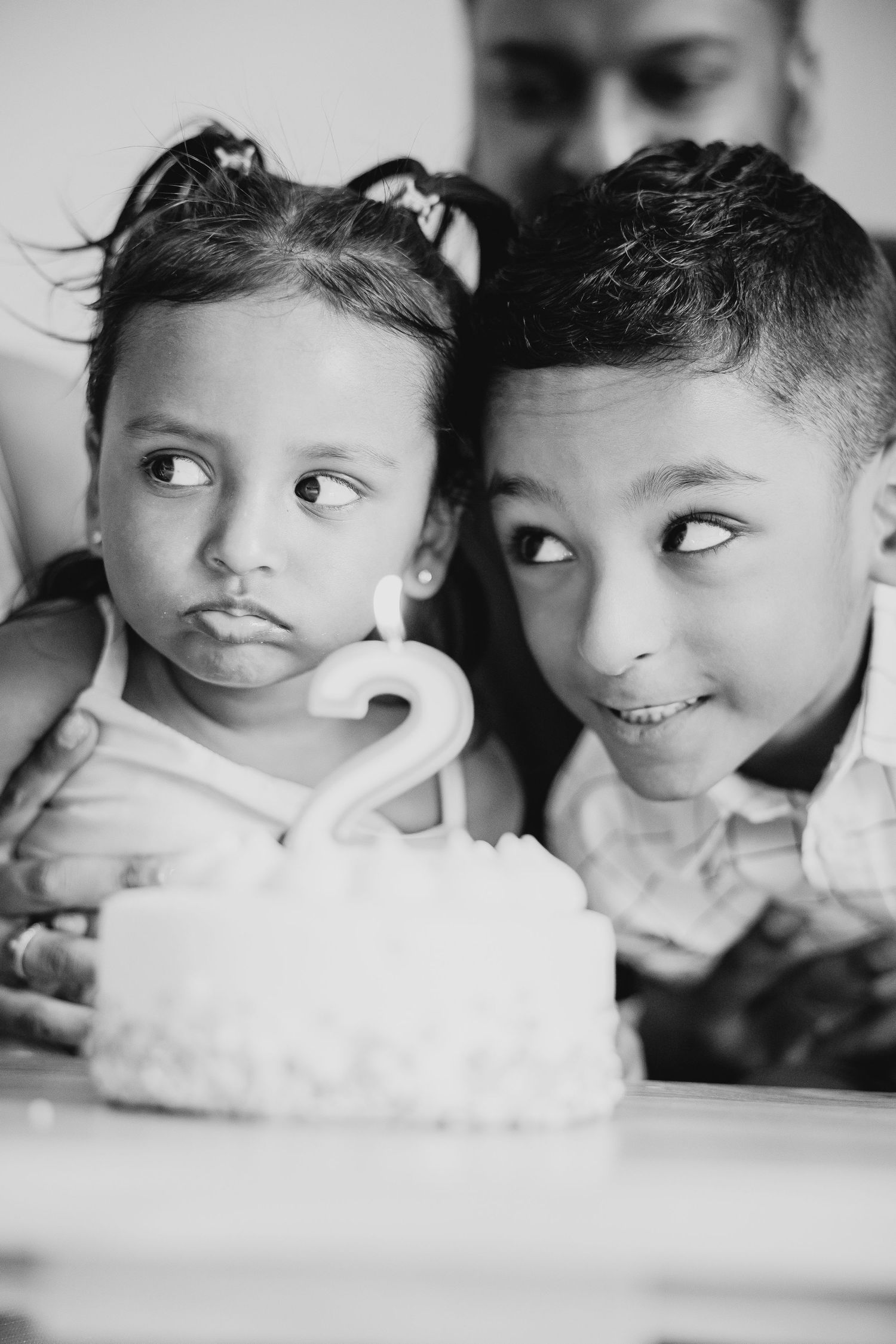 Two children lean over a birthday cake with the number 2 candle.