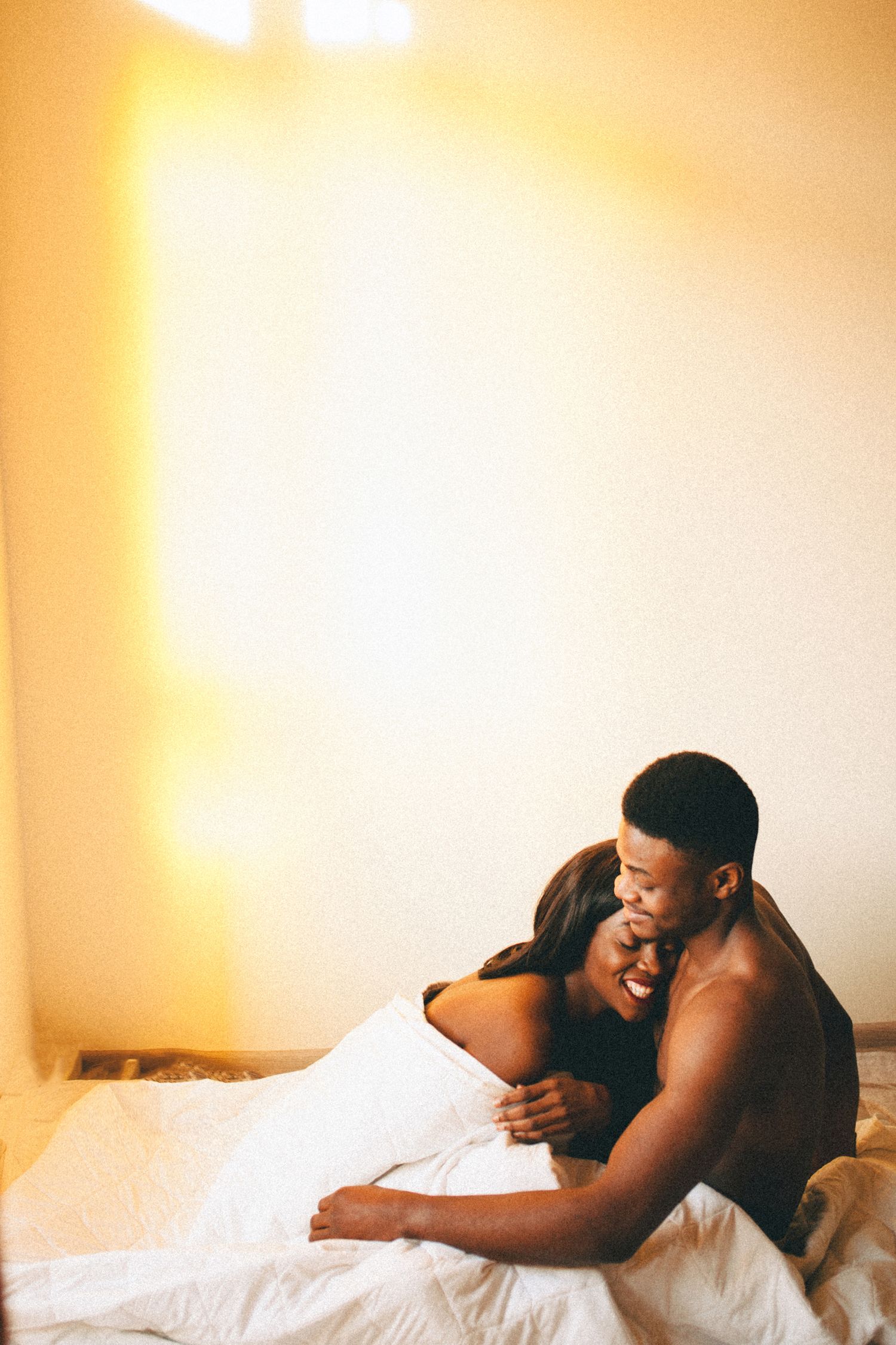 A tender moment between a couple embracing while lying in bed with warm lighting casting a golden glow.