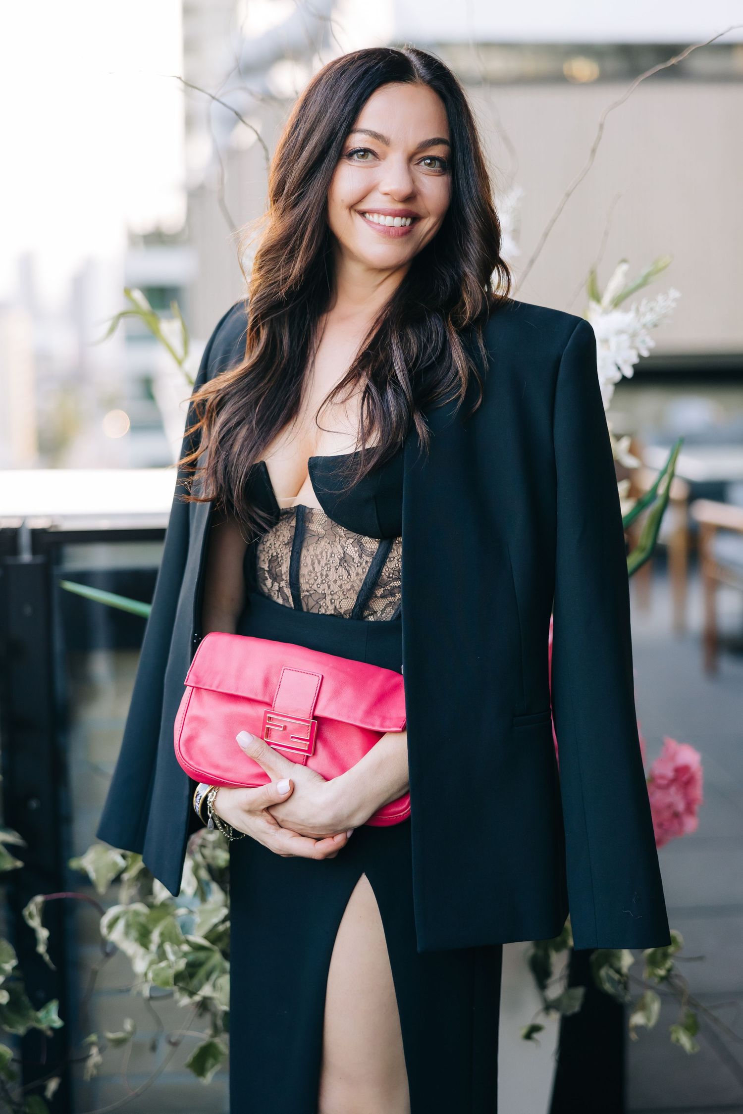Stylish outfit featuring a black blazer and dress with a vibrant pink clutch purse in an elegant setting.