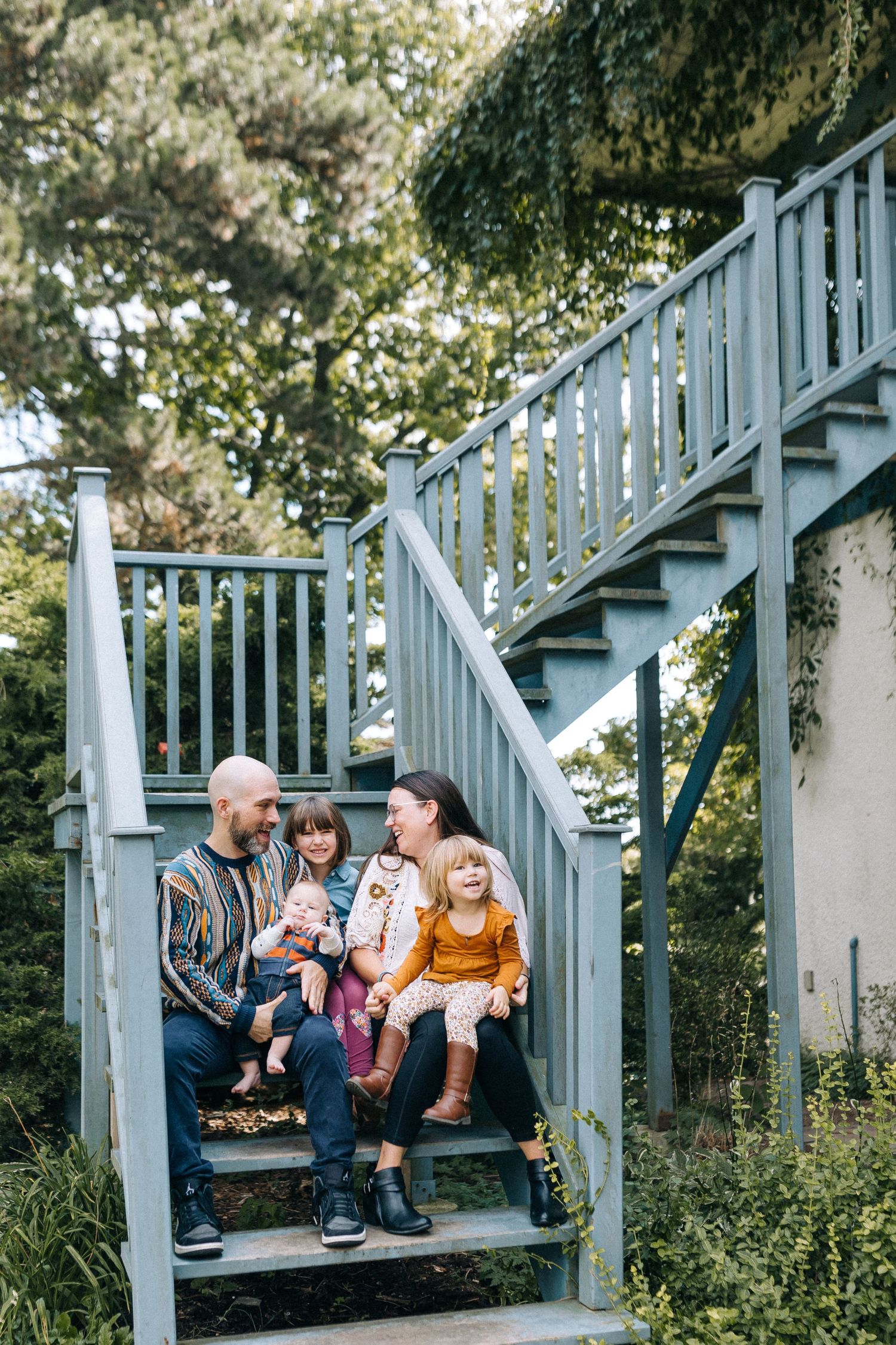 Family sitting together on outdoor gray stairs surrounded by greenery.