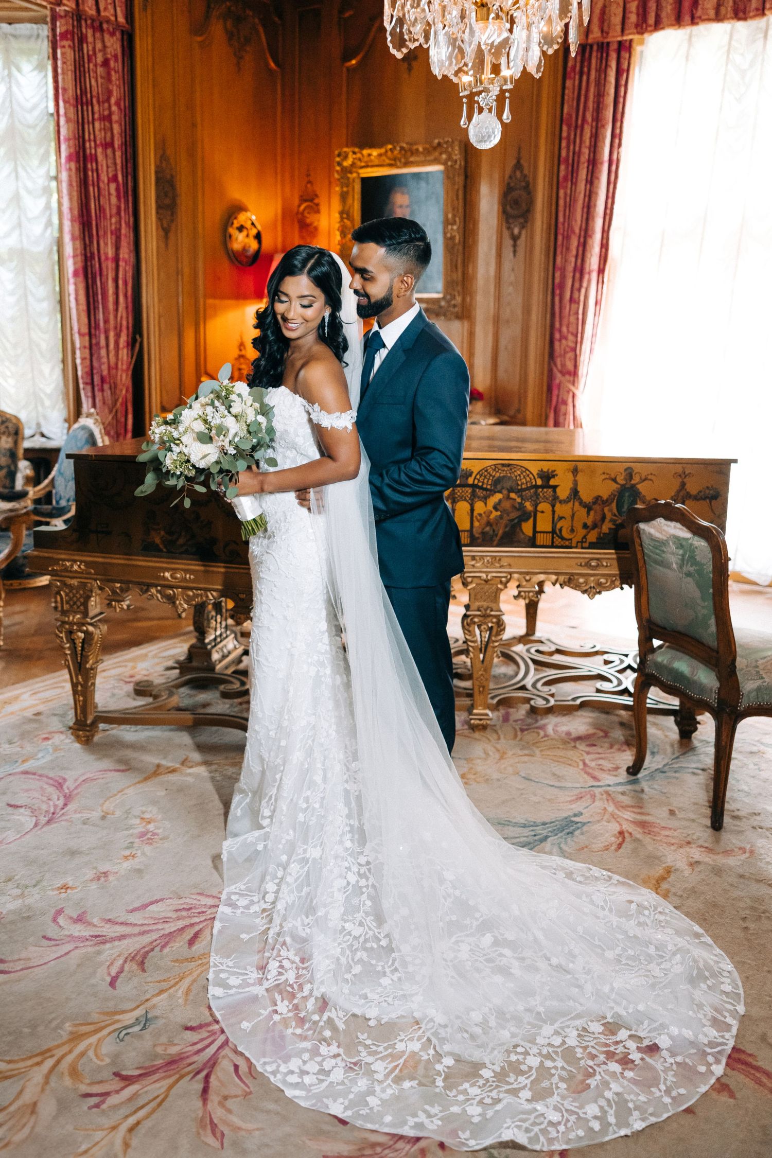 Elegant wedding portrait in ornate room with chandelier and vintage furniture.