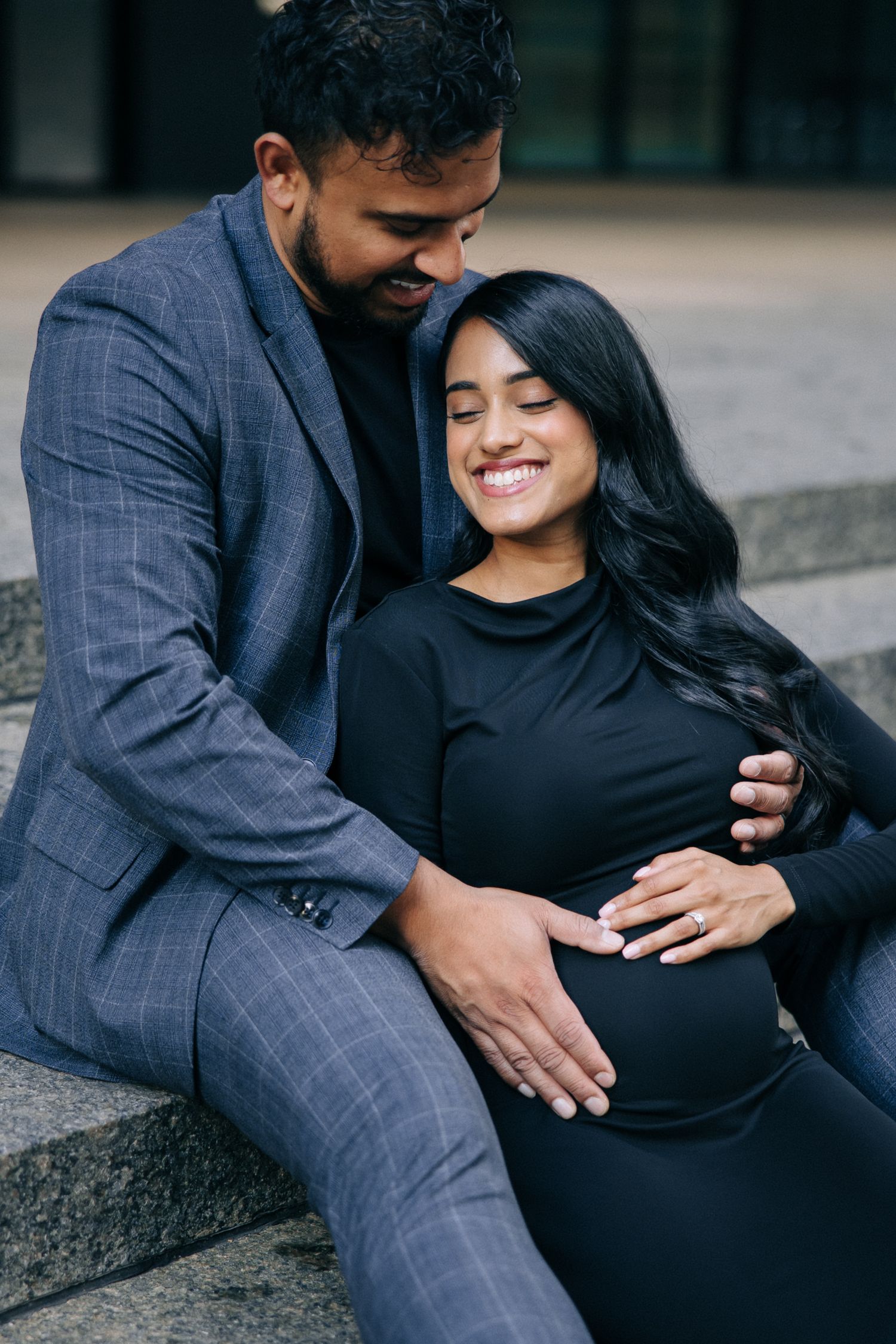 Couple shares intimate moment sitting on steps, with loving embrace and joyful smiles in urban setting.