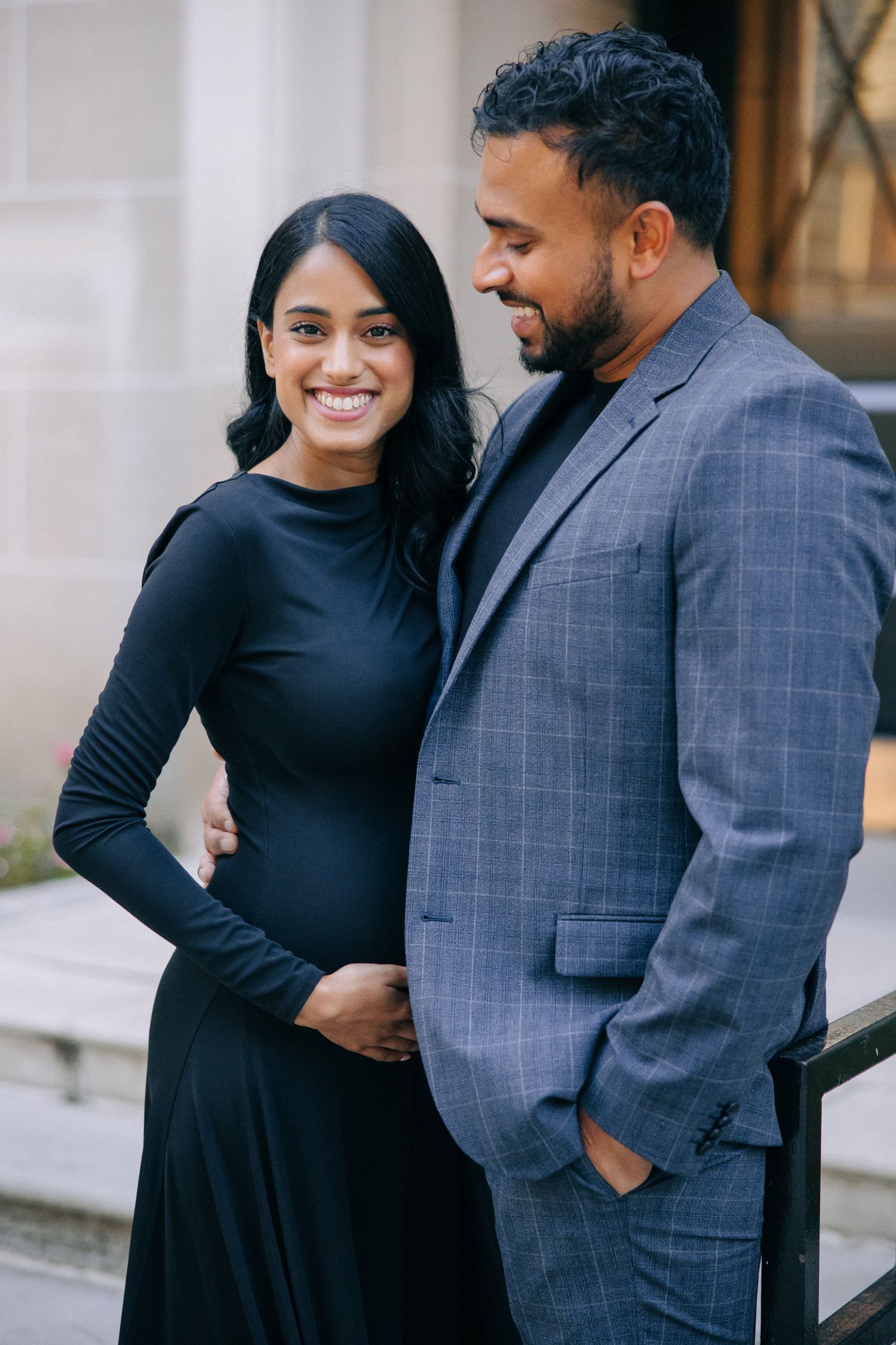 A couple shares a joyful moment together outdoors, with the woman wearing a black dress and man in a gray plaid suit.