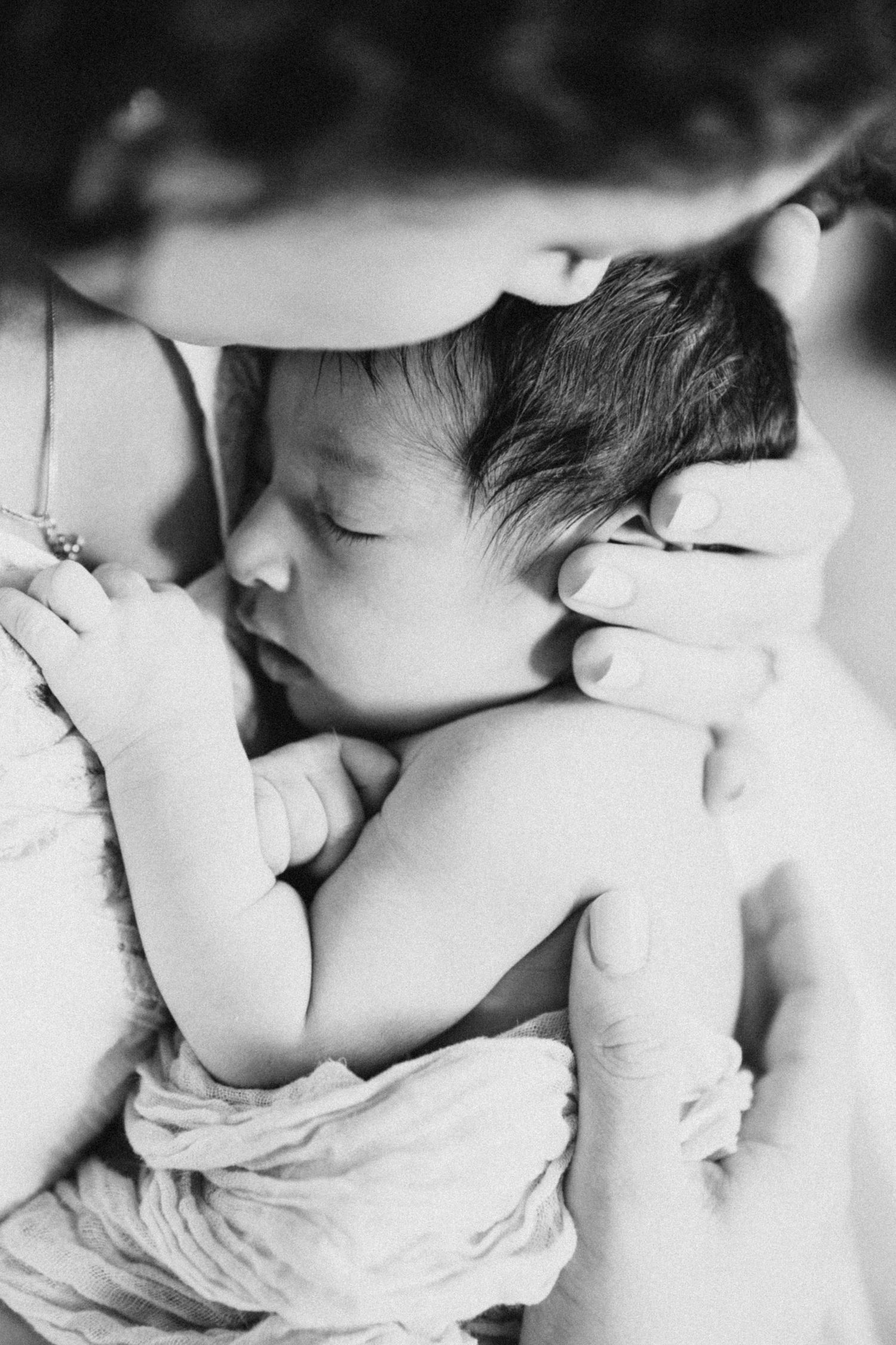 Intimate black and white portrait of a sleeping newborn being cradled gently.