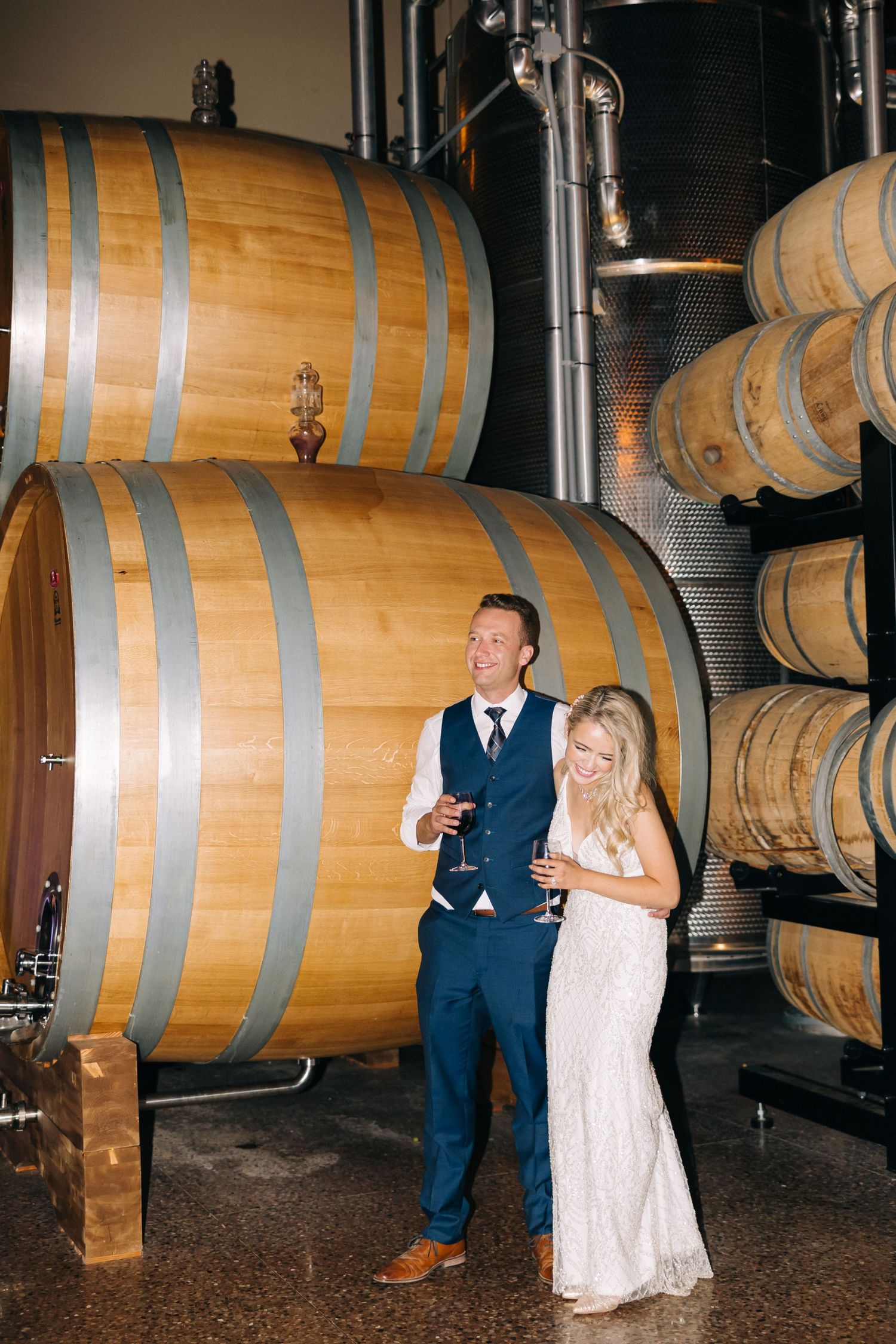 Couple in formal wear enjoying wine tasting among large oak barrels in a cellar.