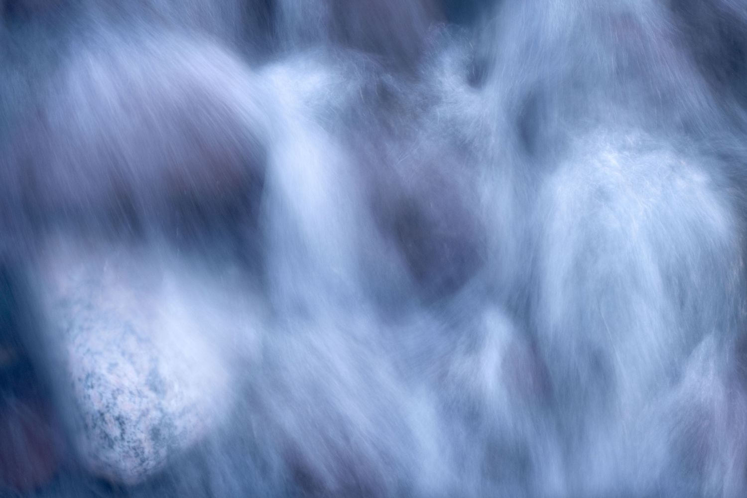Abstract long exposure of rushing water creating a misty, ethereal blue-toned effect.