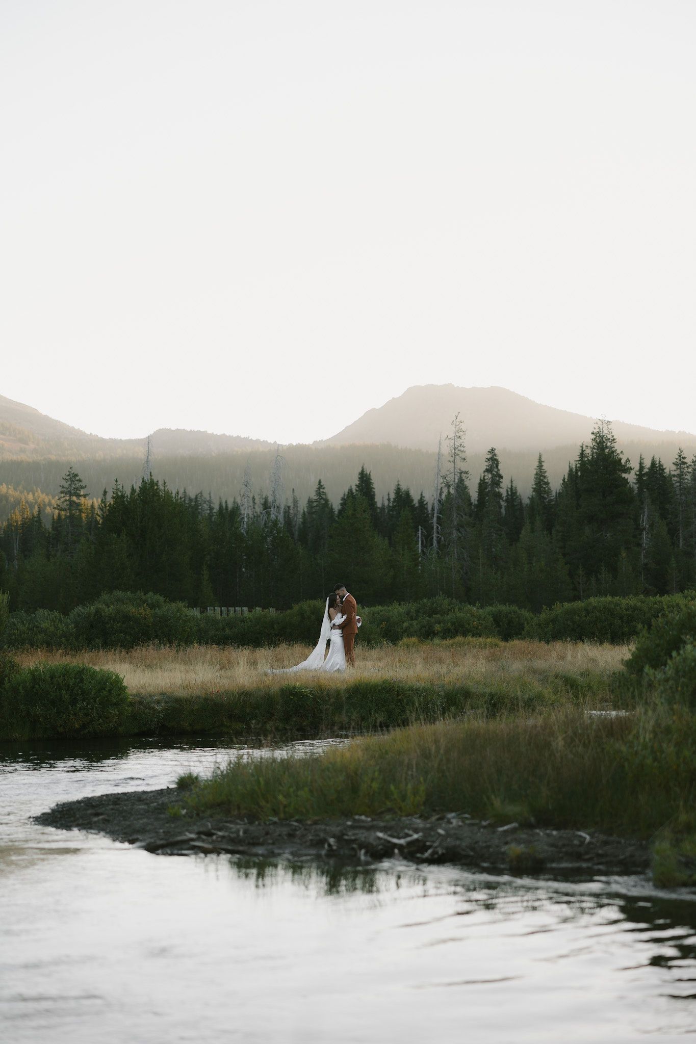 A wide landscape sunrise shot of Oregon model couple, Avery and Javan Darling. There's a creek in the foreground and mountains in the back.