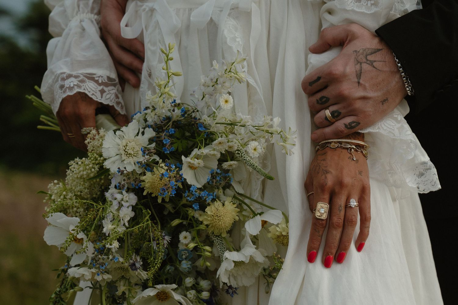 Close-up details of a wedding ceremony showing floral arrangements, white lace dress fabric, and hands with rings.