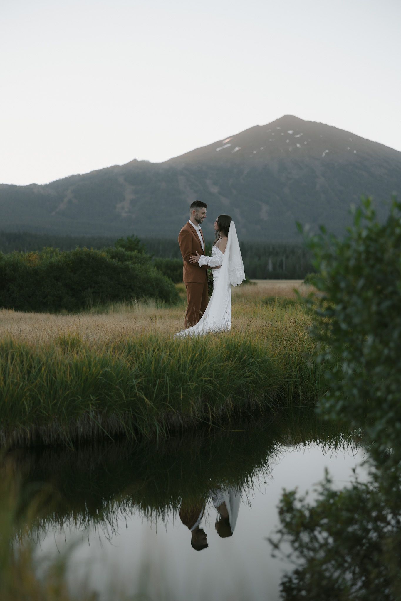 Oregon model couple, Avery and Javan Darling, stand near a creek with their reflection during a sunrise elopement shoot.