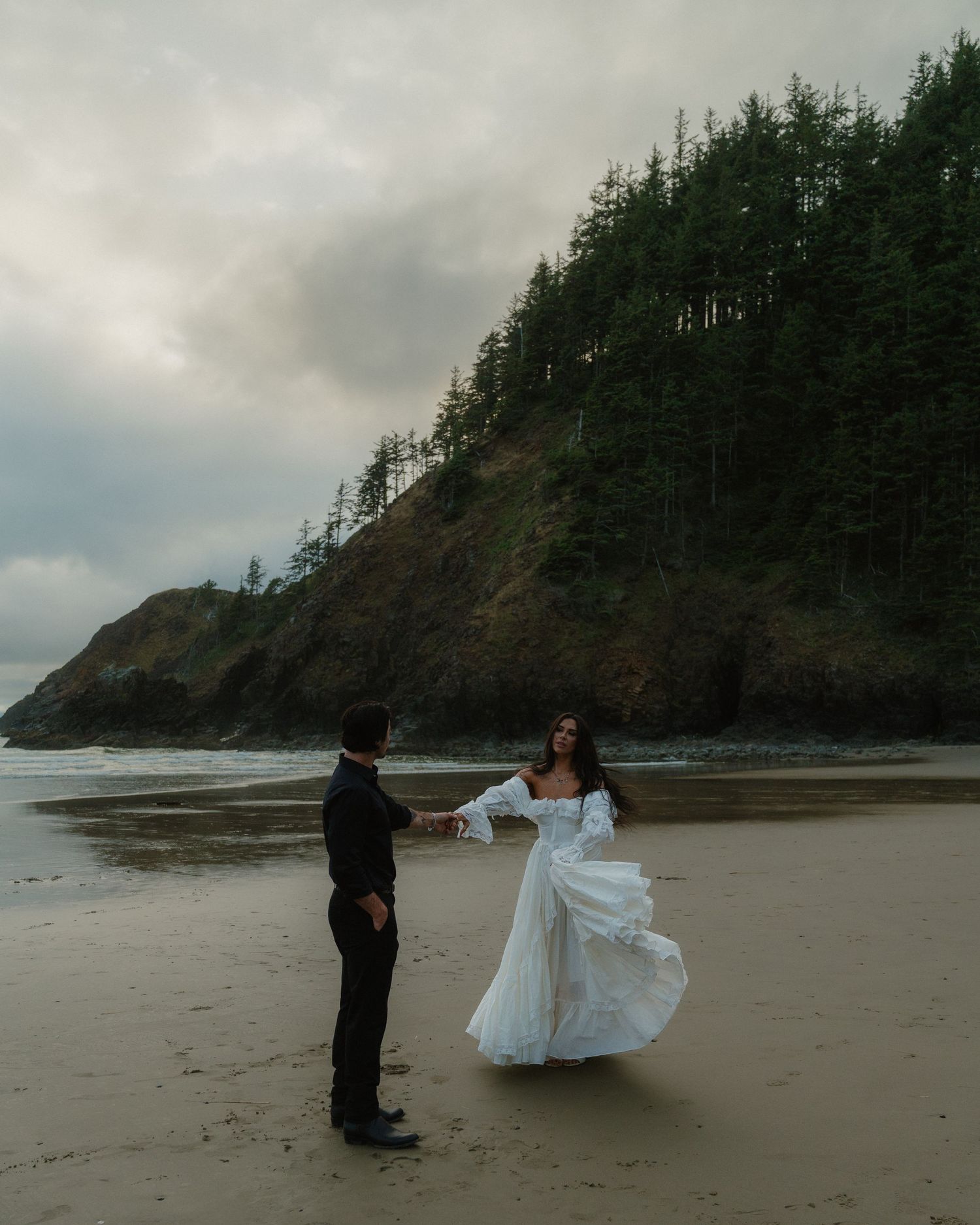 Moody coastal landscape with dramatic cliffs and evergreen trees along a misty Pacific Northwest beach at sunset.