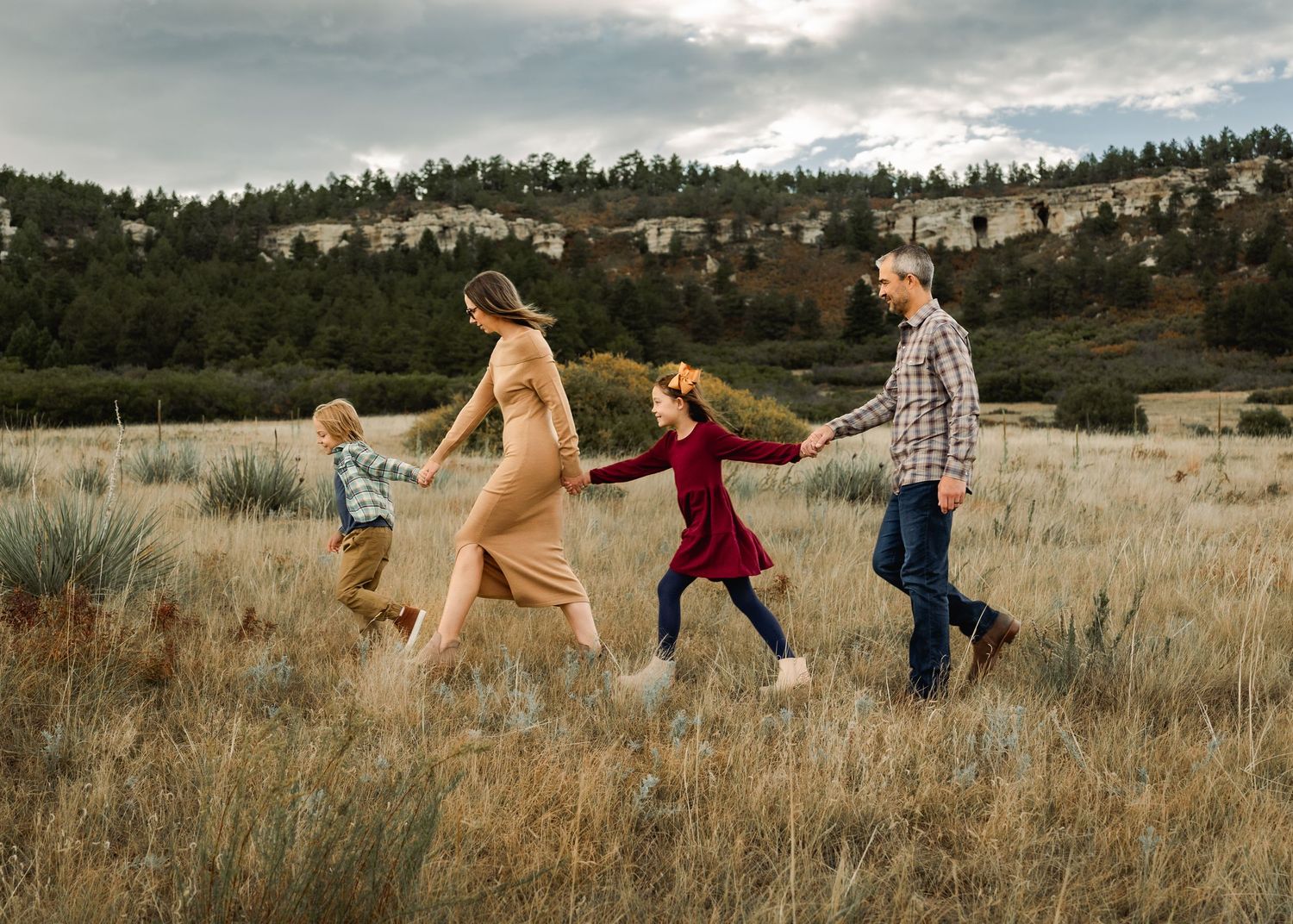Family running and playing together in a golden grass field during sunset.