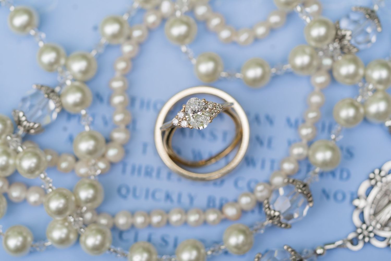 Wedding rings displayed on a blue background surrounded by pearl necklaces and crystal accents.