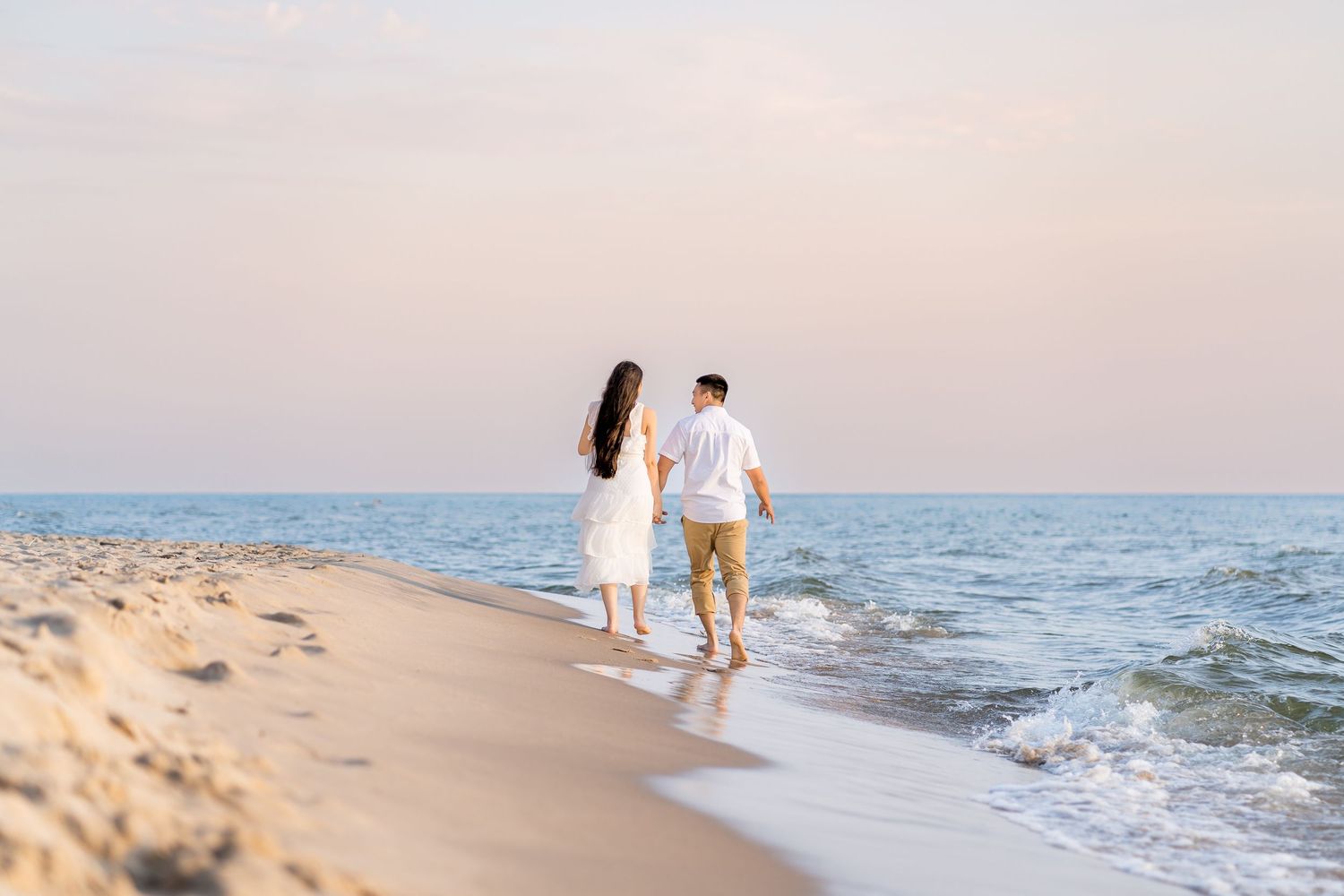 A couple walking along a sandy beach at sunset holding hands and leaving footprints in the wet sand.