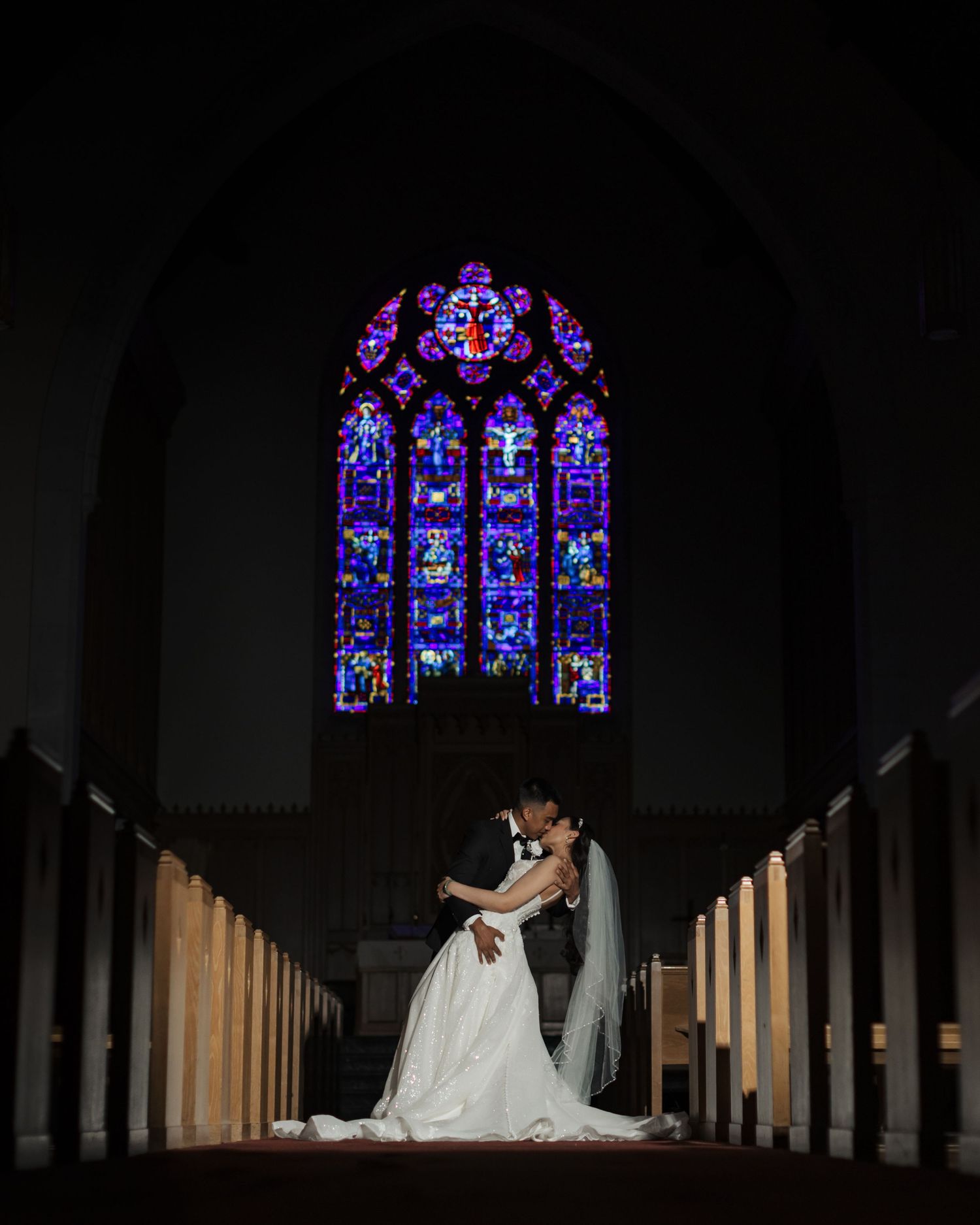 Two people share a romantic moment in a church with stunning blue stained glass windows illuminating the scene.