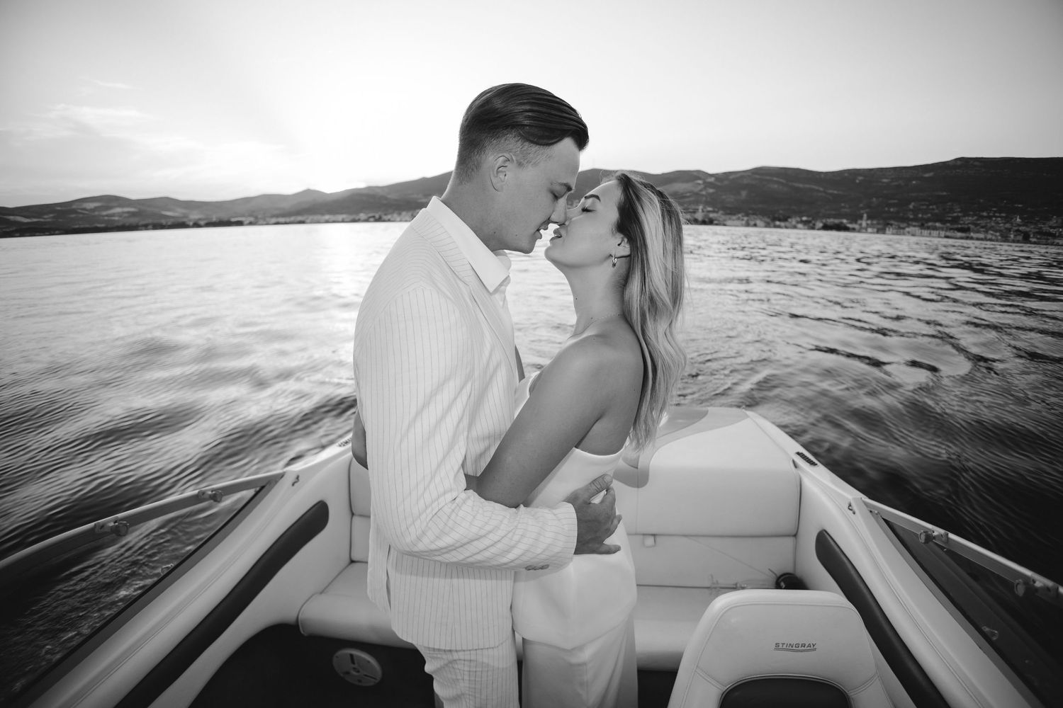 Romantic couple sharing intimate moments while sailing on a boat at sunset over tranquil waters.