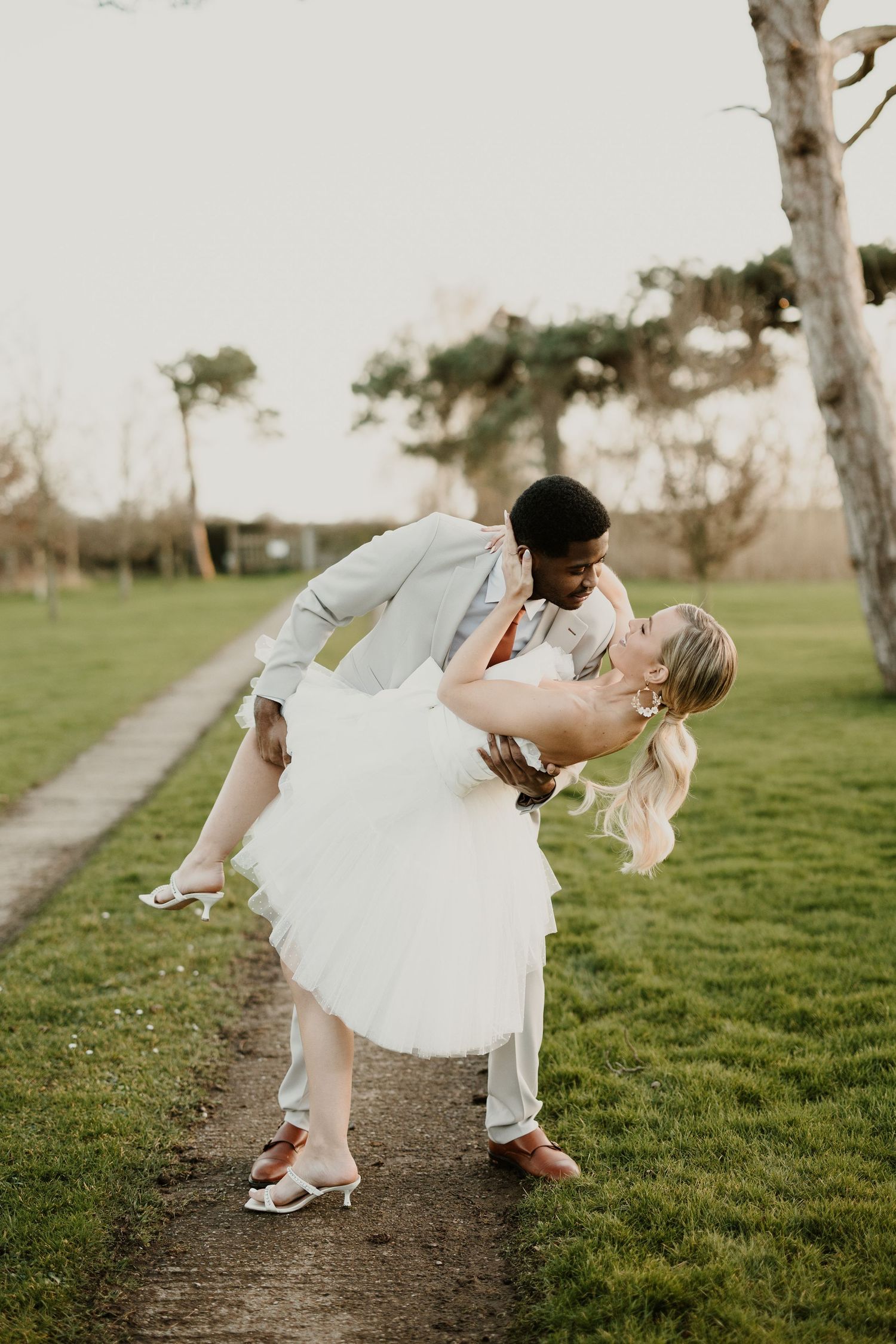 Romantic dip kiss sequence in white wedding attire against green grass field.