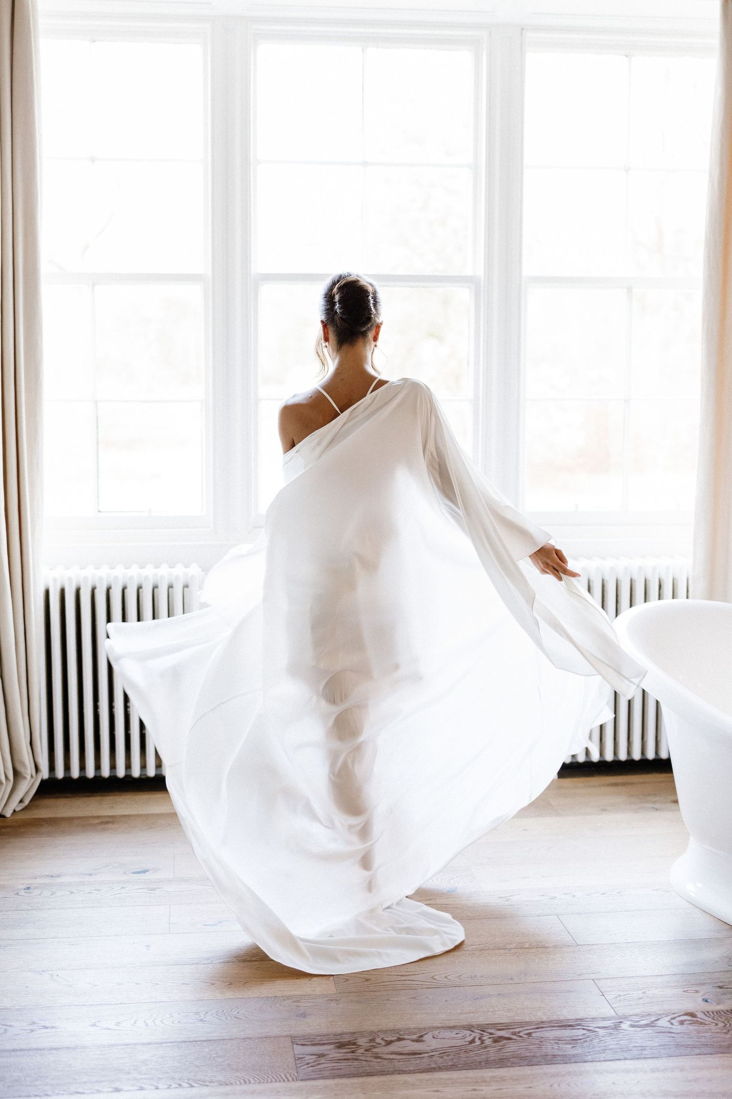 Figure in flowing white fabric creates ethereal motion sequence against bright minimalist studio space.