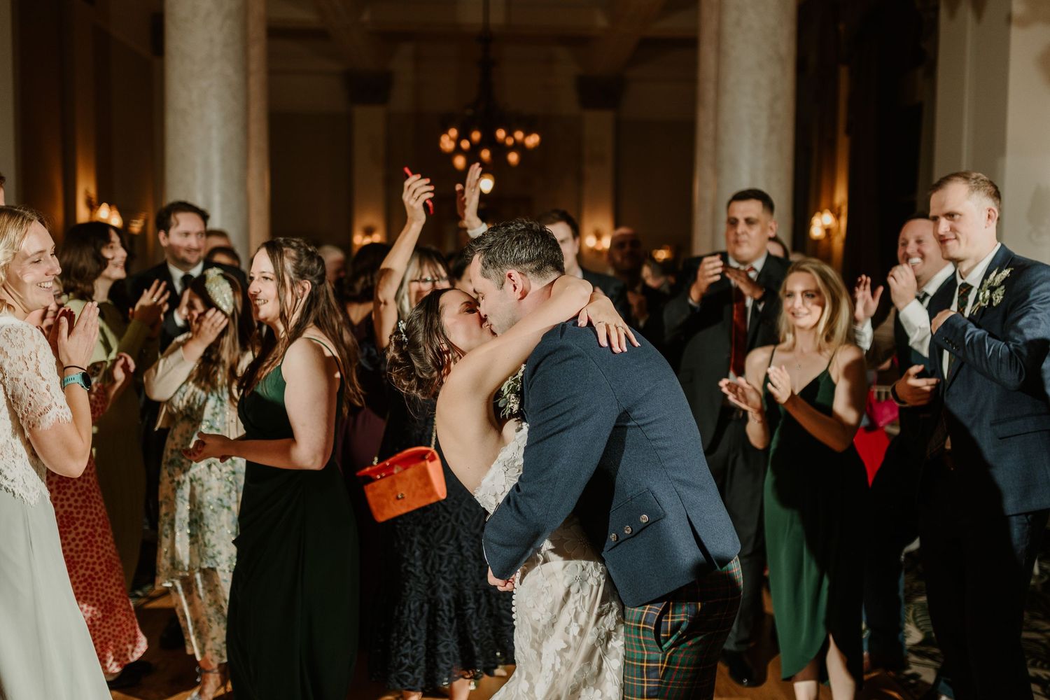 Couple shares romantic embrace during first dance at wedding reception while guests applaud and capture the moment.