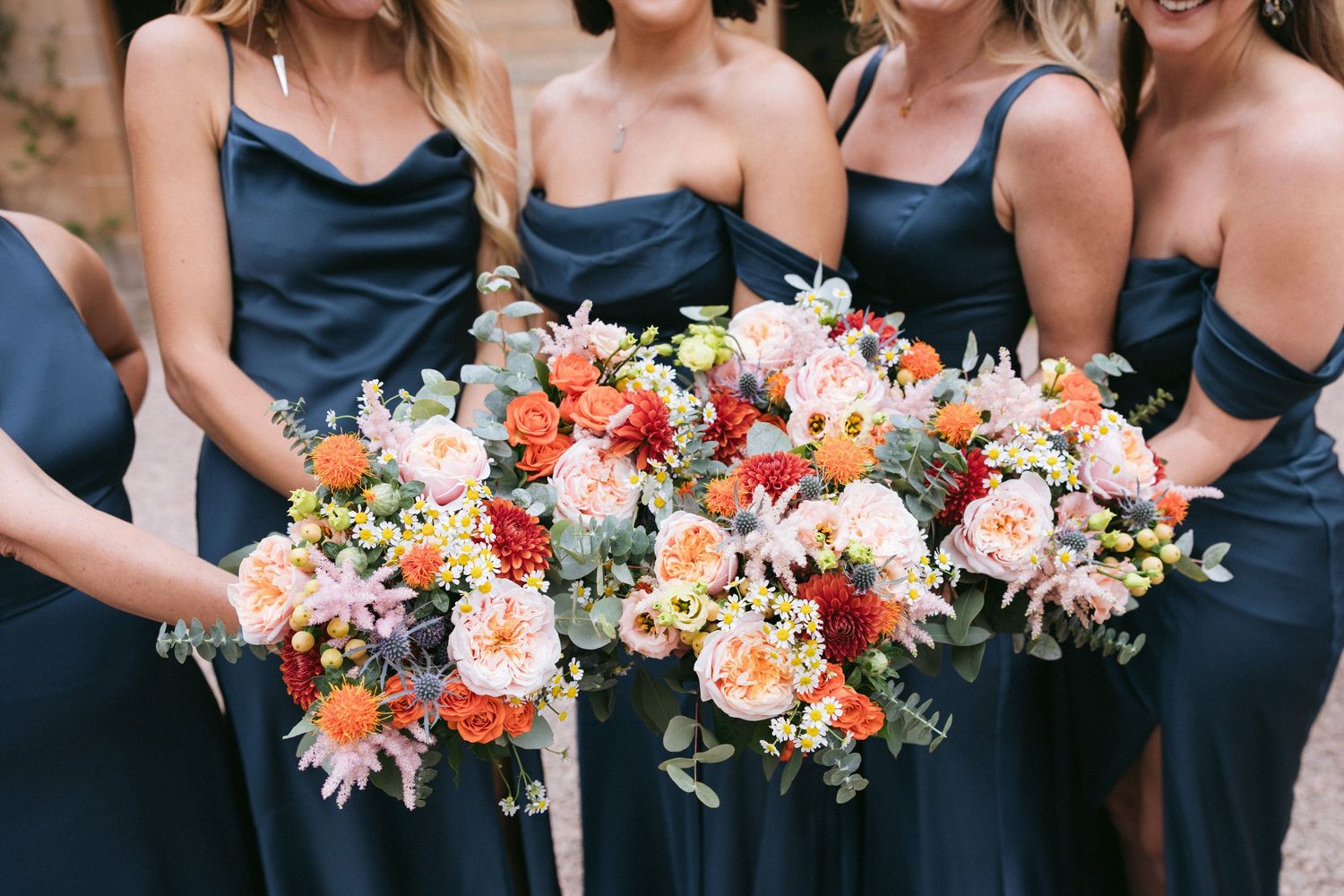 Row of elegant floral bouquets featuring peach, pink and white blooms against navy blue dresses.