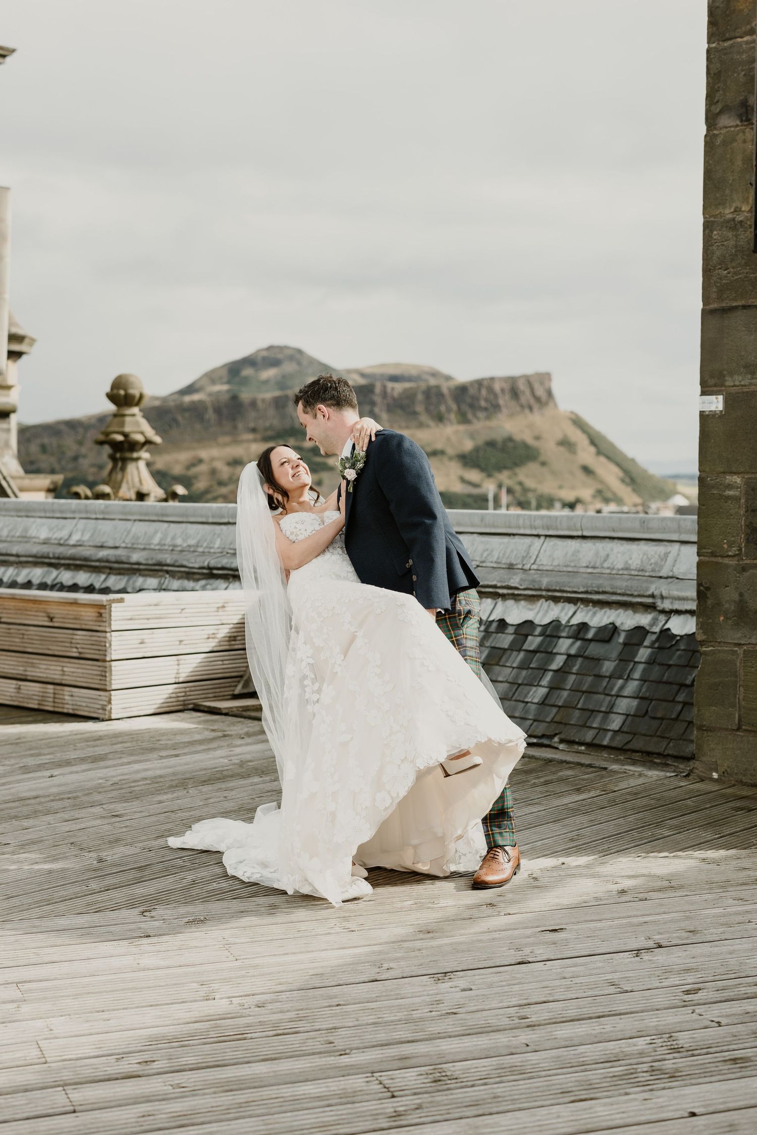 A romantic couple in wedding attire sharing an intimate moment on a wooden deck with mountains in the background.