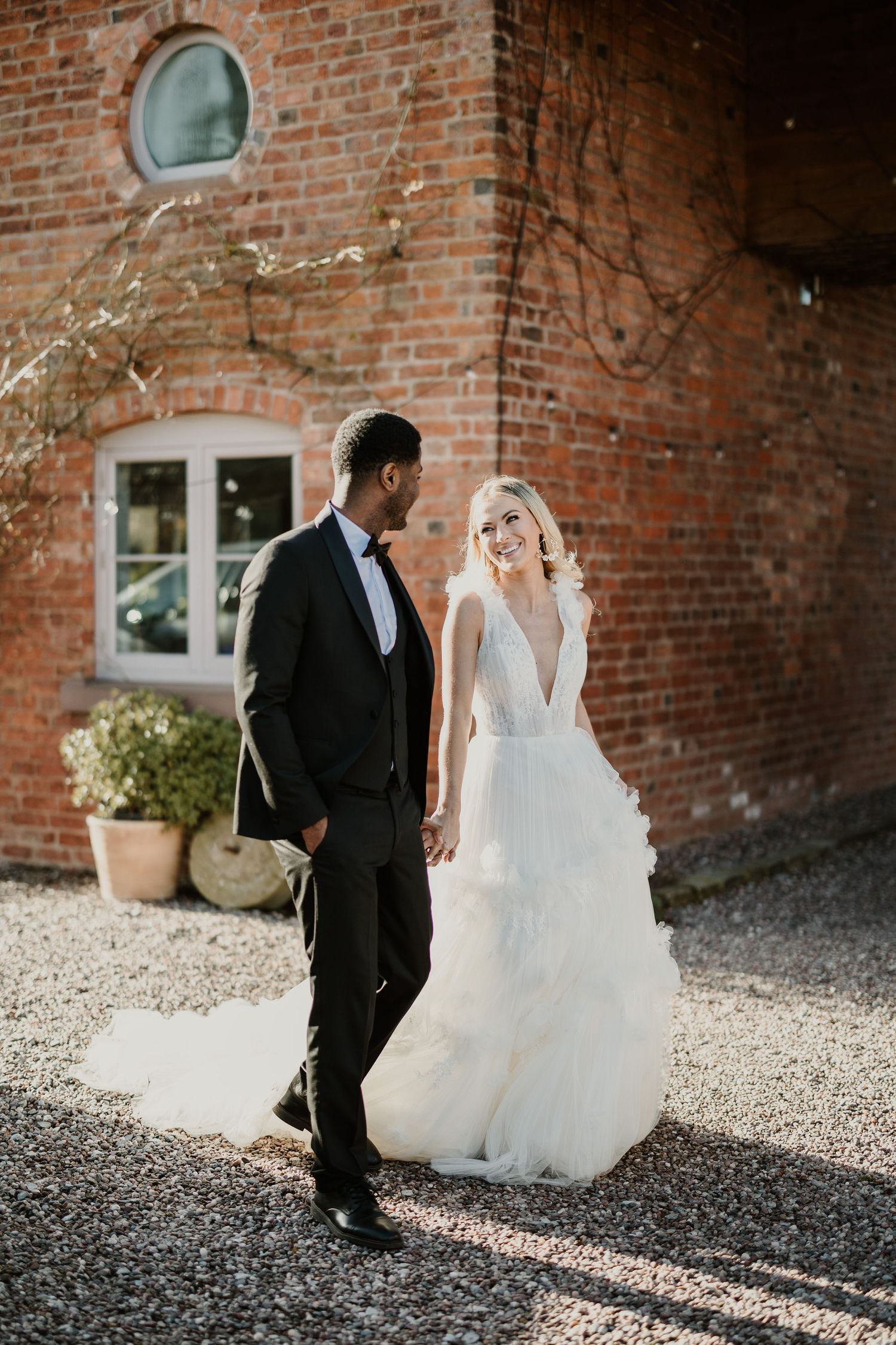 A romantic wedding couple poses against a rustic brick wall backdrop in elegant attire.