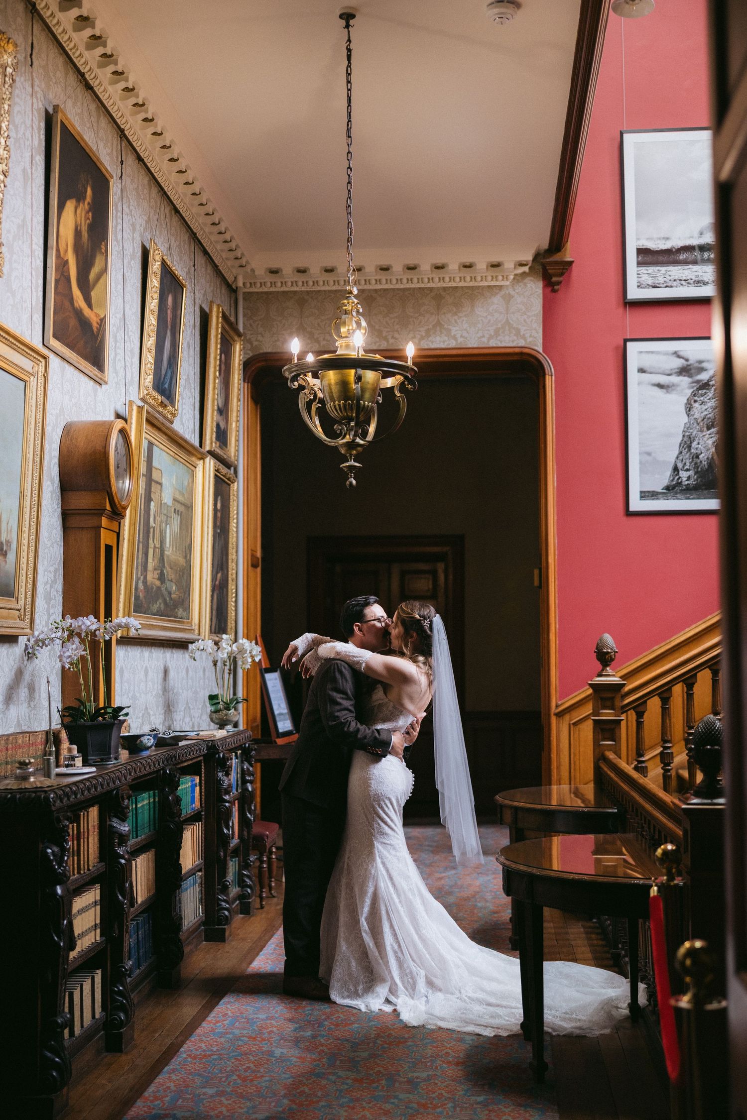 Elegant wedding photos showing a bride in white dress walking through a historic mansion hallway with red walls and artwork.