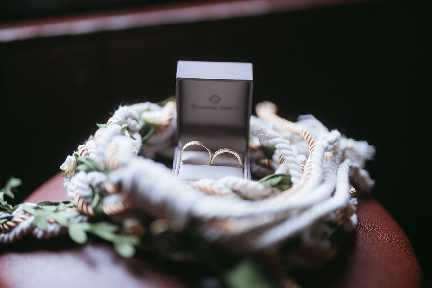 Wedding rings displayed in a gray box with delicate floral and greenery accents.