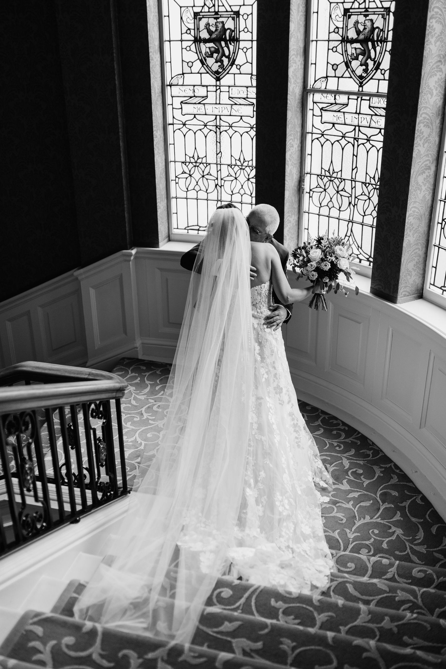 Elegant bridal veil trailing on patterned carpet by ornate stained glass windows in black and white photo series.