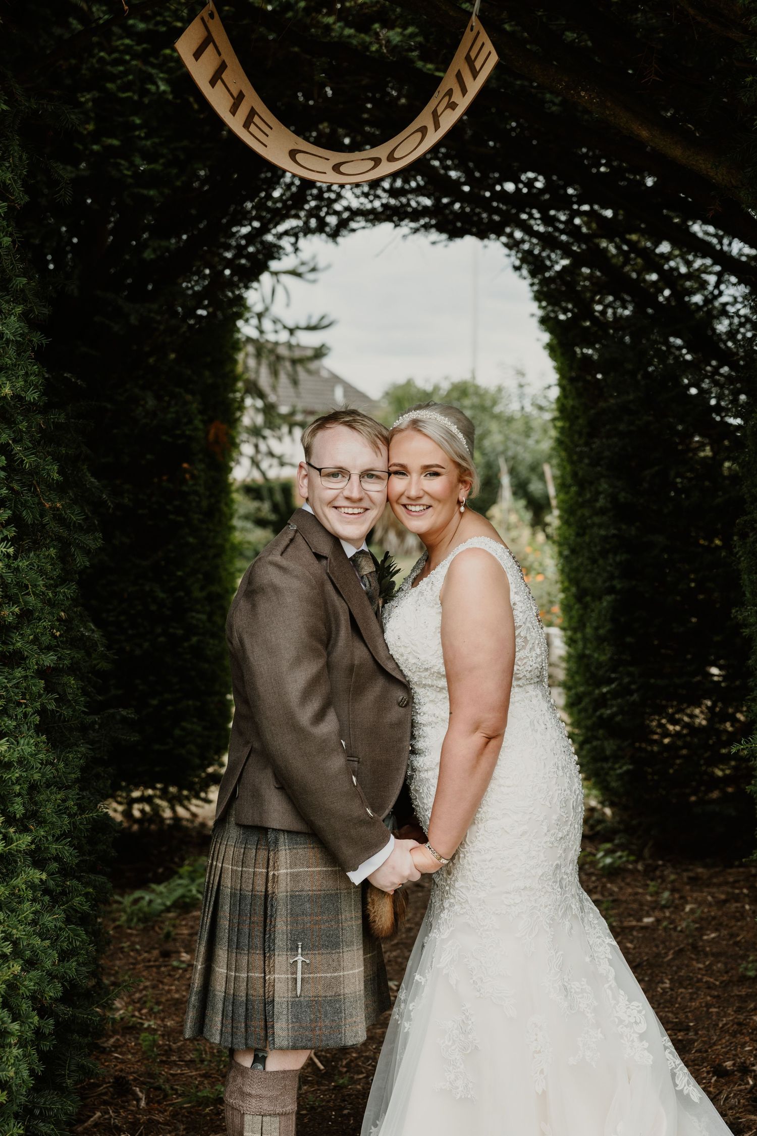 A couple shares an intimate moment under a tree canopy during their Scottish-themed wedding ceremony.