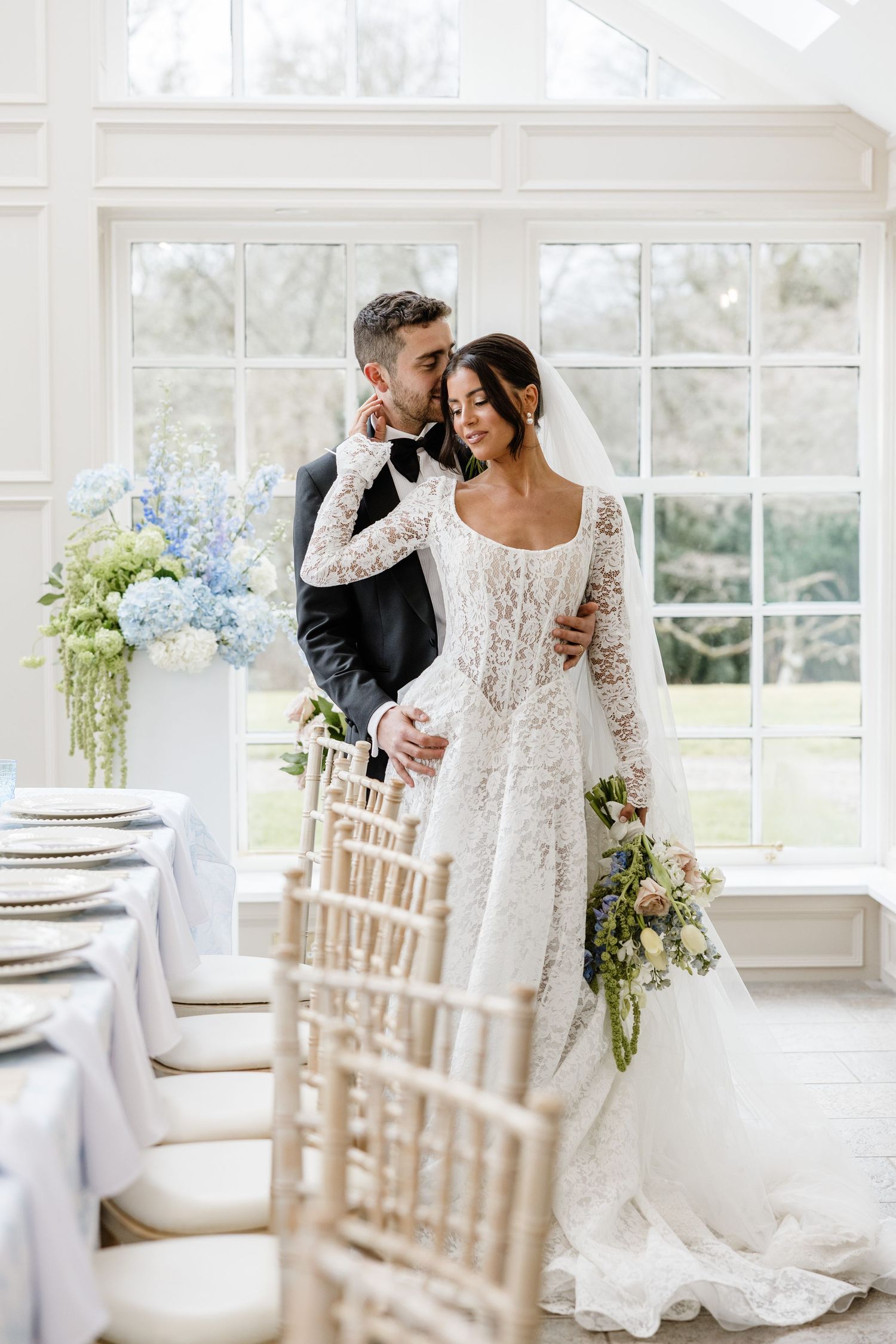 An elegant wedding reception setup in a bright white room with chiavari chairs and floral arrangements.