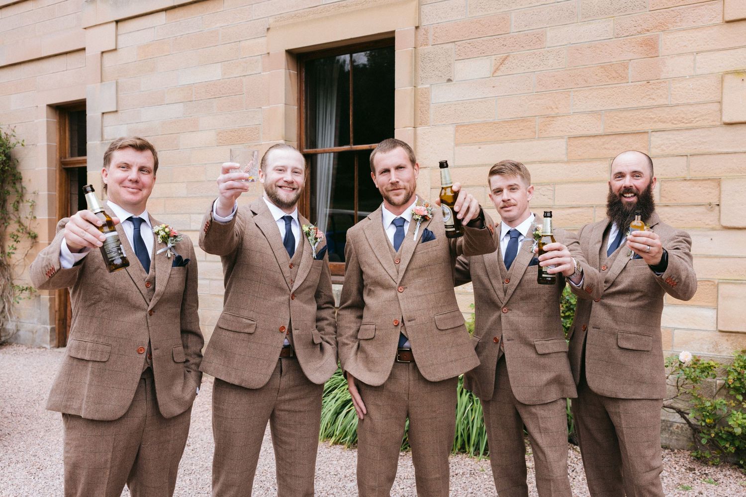 A group in matching brown suits and blue ties pose together in a line against a wooden wall.