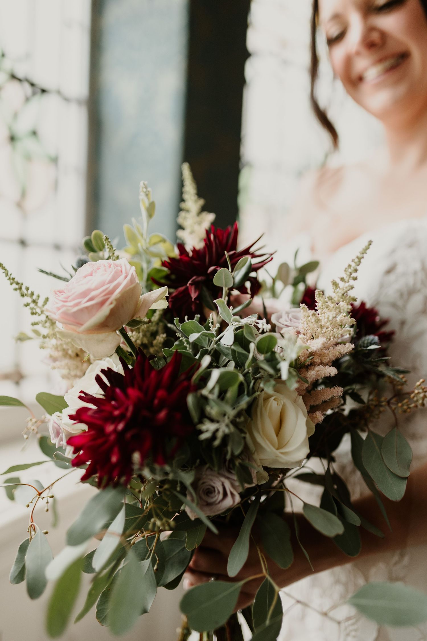 Close-up of romantic bridal bouquet featuring burgundy dahlias and blush roses with eucalyptus.