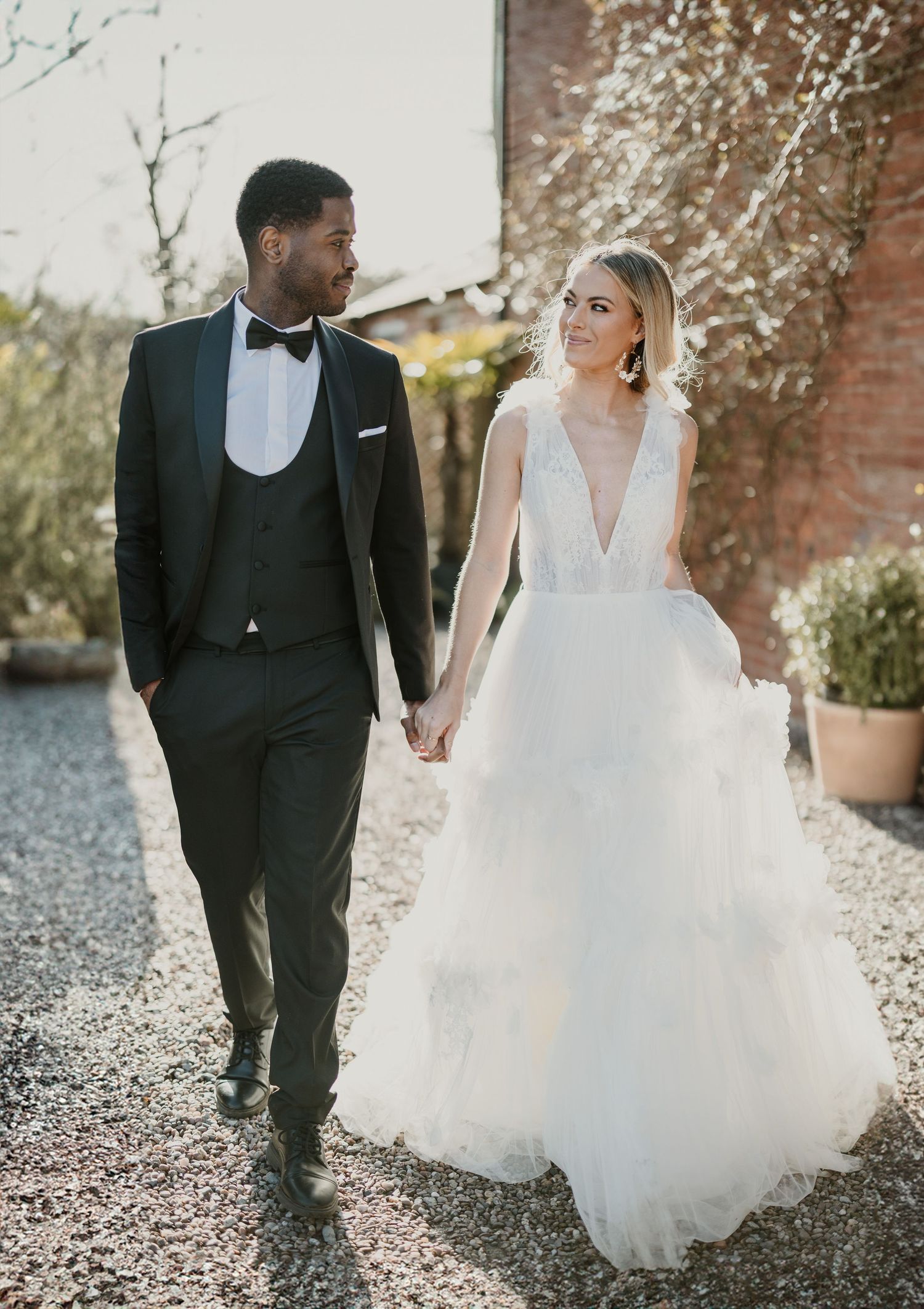 Black and white wedding couple walk together on gravel path in romantic outdoor setting.