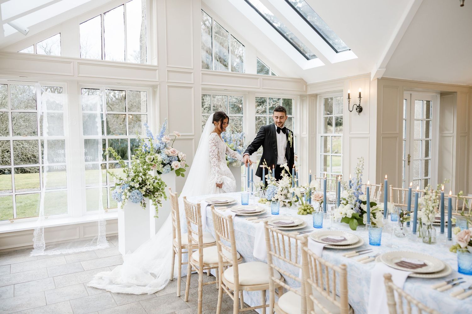 A bright conservatory wedding venue with white decor, glass ceiling, and elegant table settings for a reception.