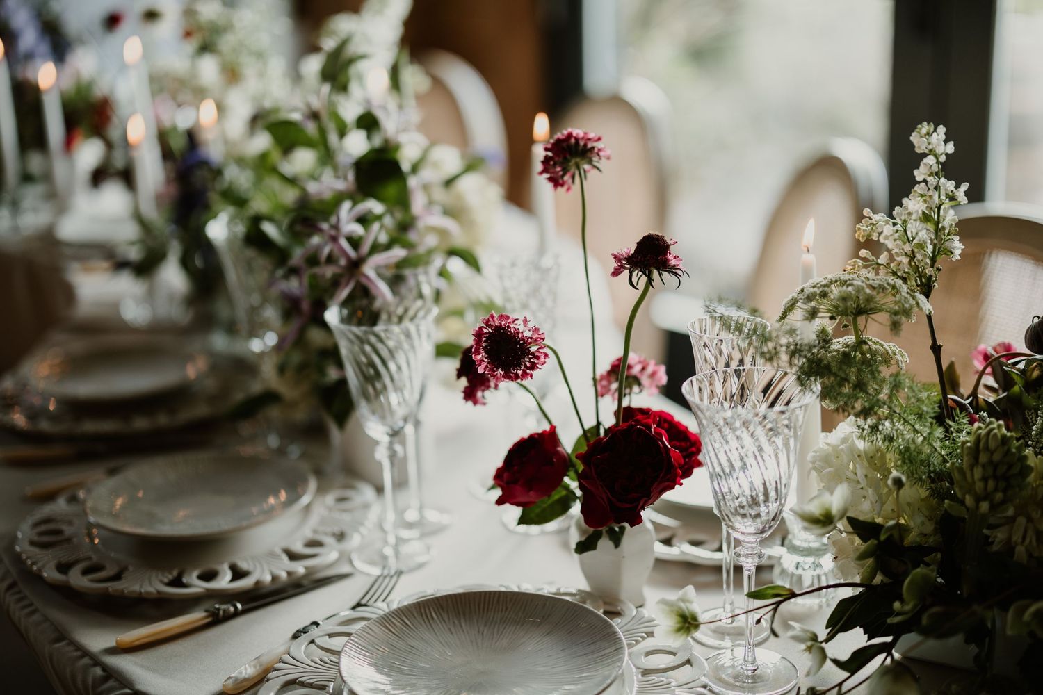 Elegant wedding table setting with deep red flowers and crystal glassware.