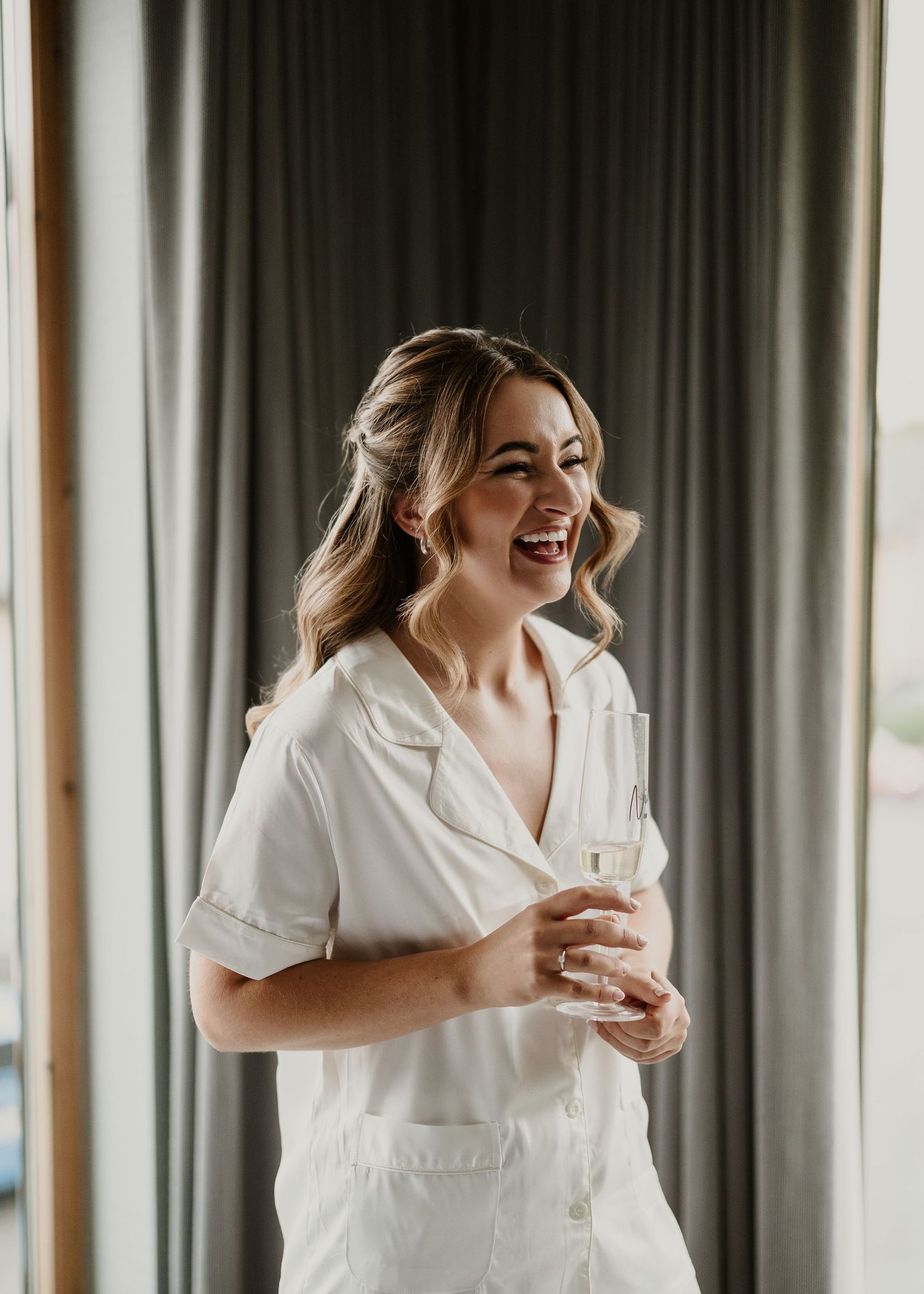 A joyful moment captured as someone in a white button-down shirt laughs while holding a glass.