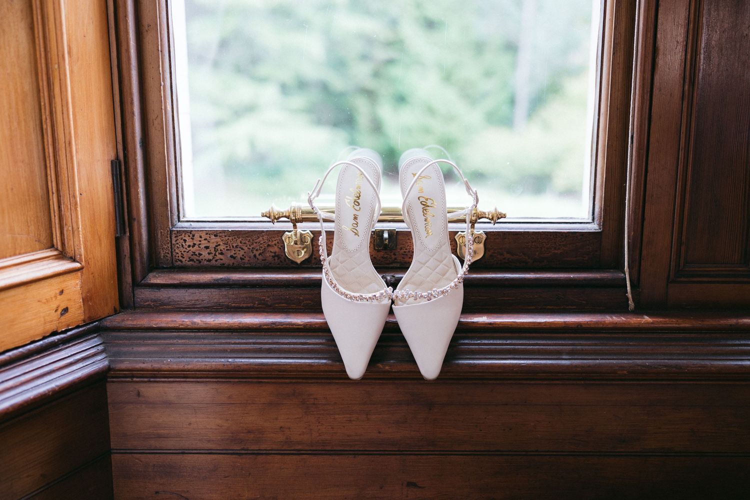 White wedding shoes and decor items arranged on a rustic wooden surface near a window.