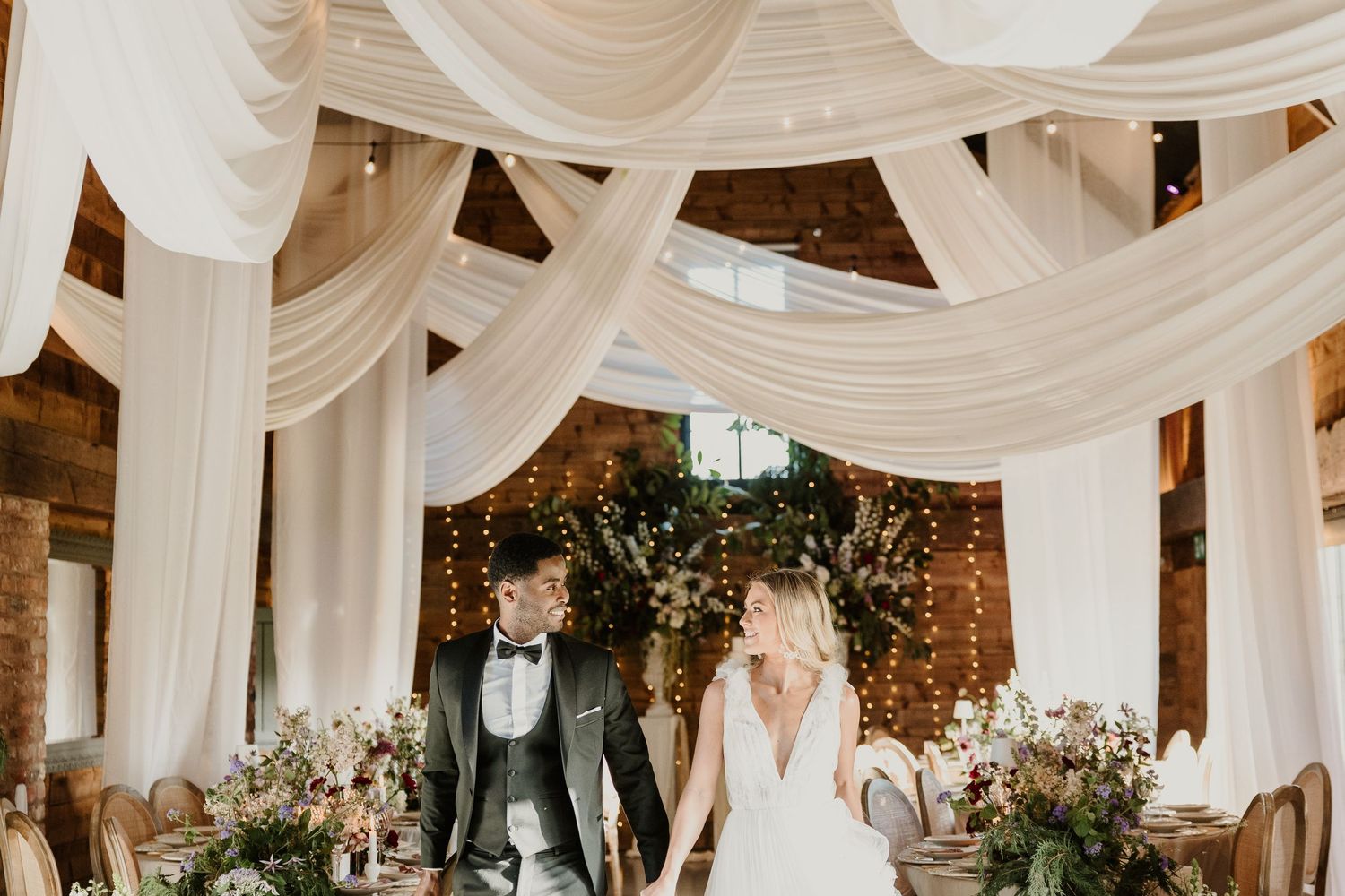 Elegant wedding ceremony under draped white fabric with floral arrangements in a rustic venue.