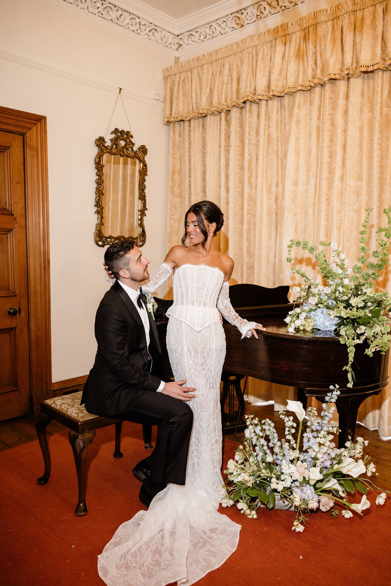 Romantic wedding couple dancing in an elegant room decorated with floral arrangements and gold curtains.
