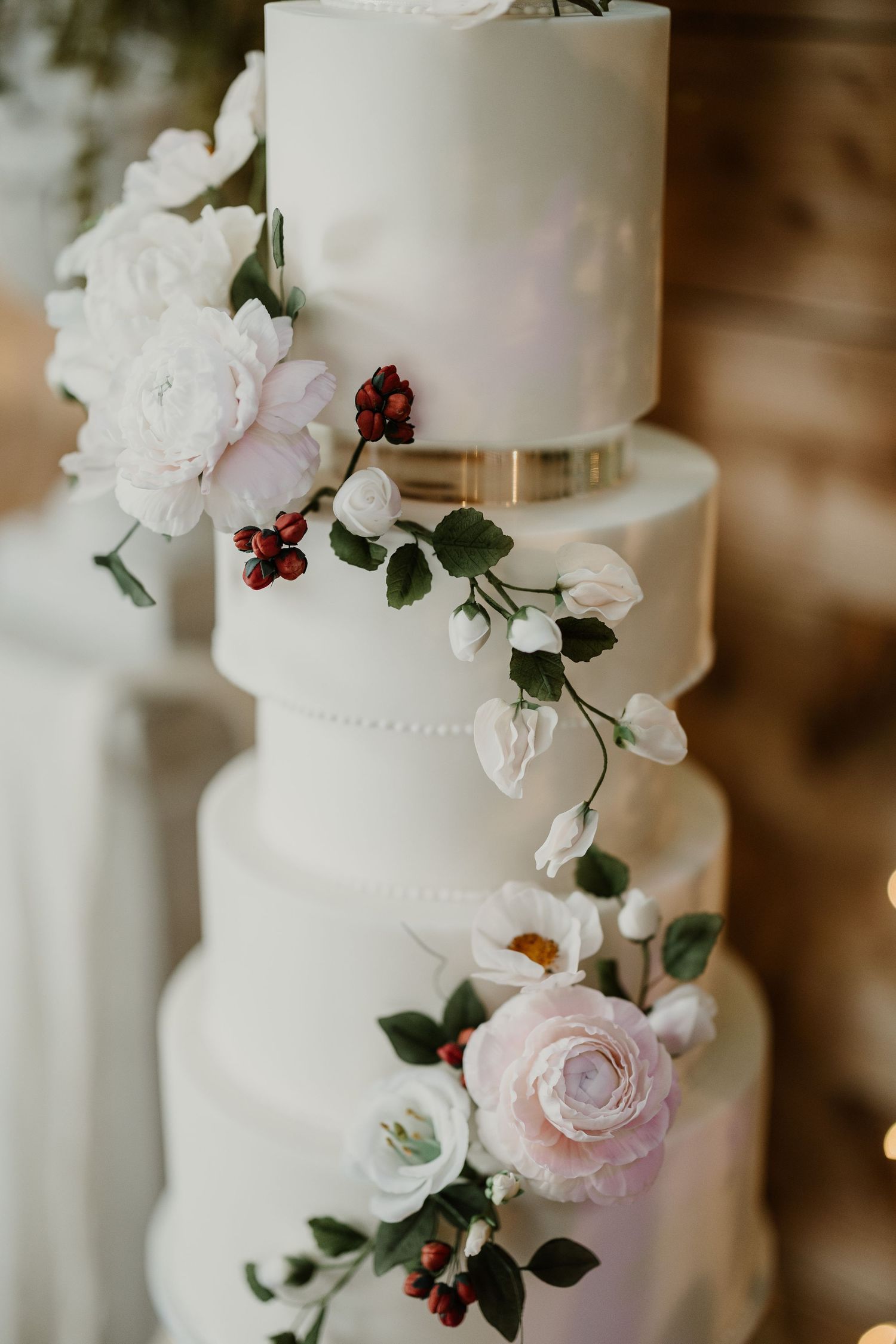 White tiered wedding cake decorated with delicate pink roses and burgundy florals.