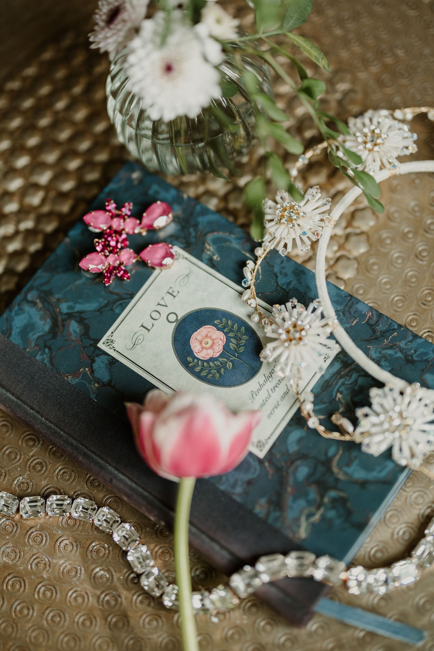 Vintage book with flowers and delicate jewelry on textured surface.