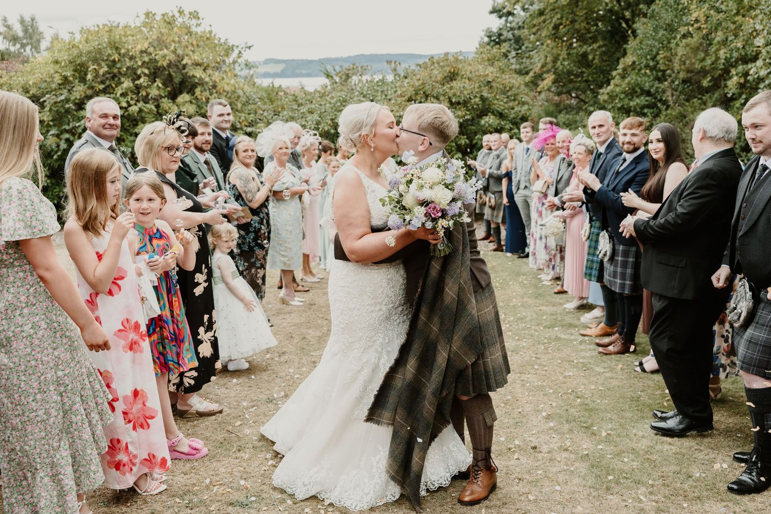 Wedding guests line the pathway throwing confetti as the newlyweds walk through during an outdoor celebration.