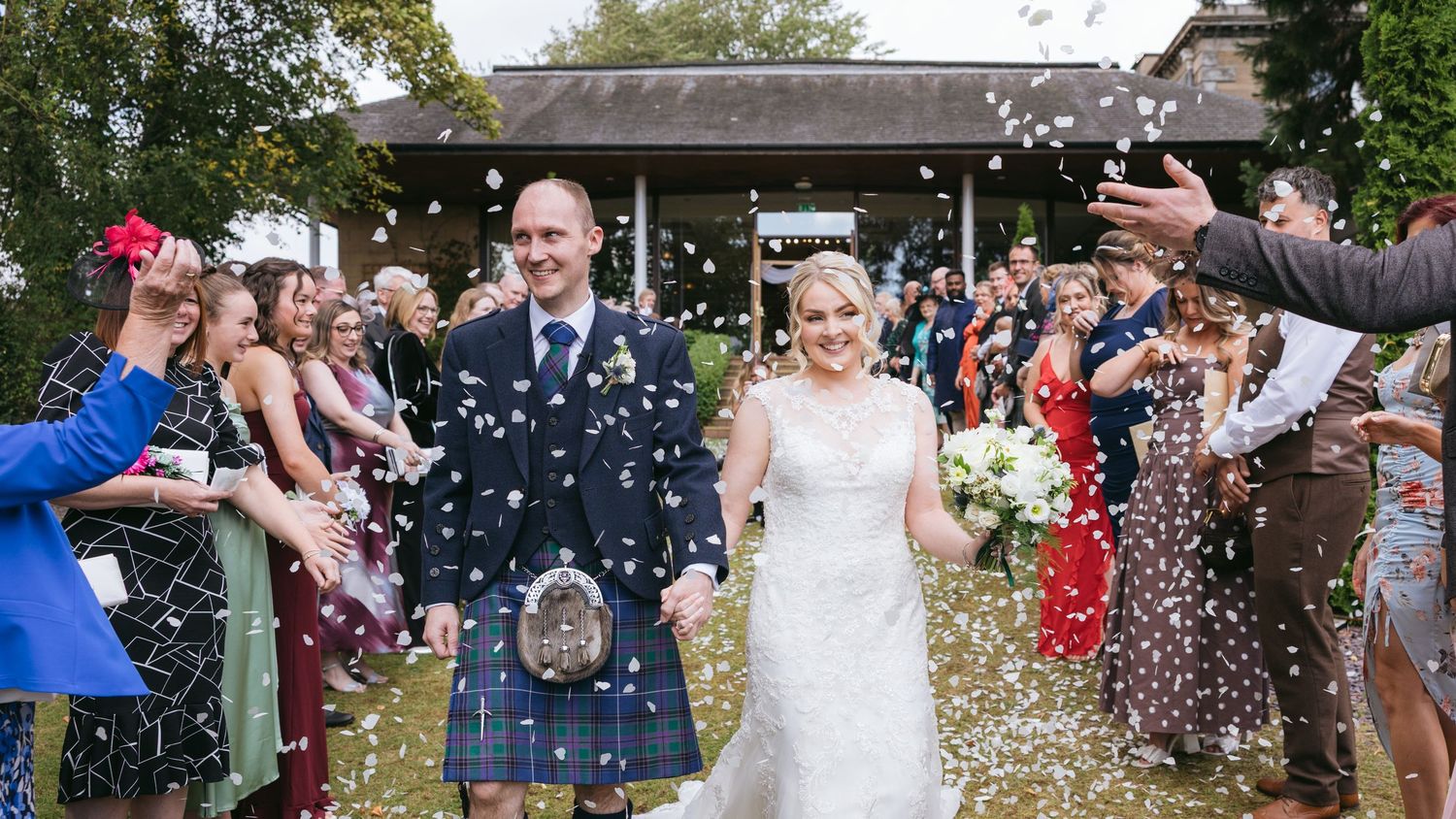 Happy couple walks through shower of confetti from wedding guests outside venue after ceremony.